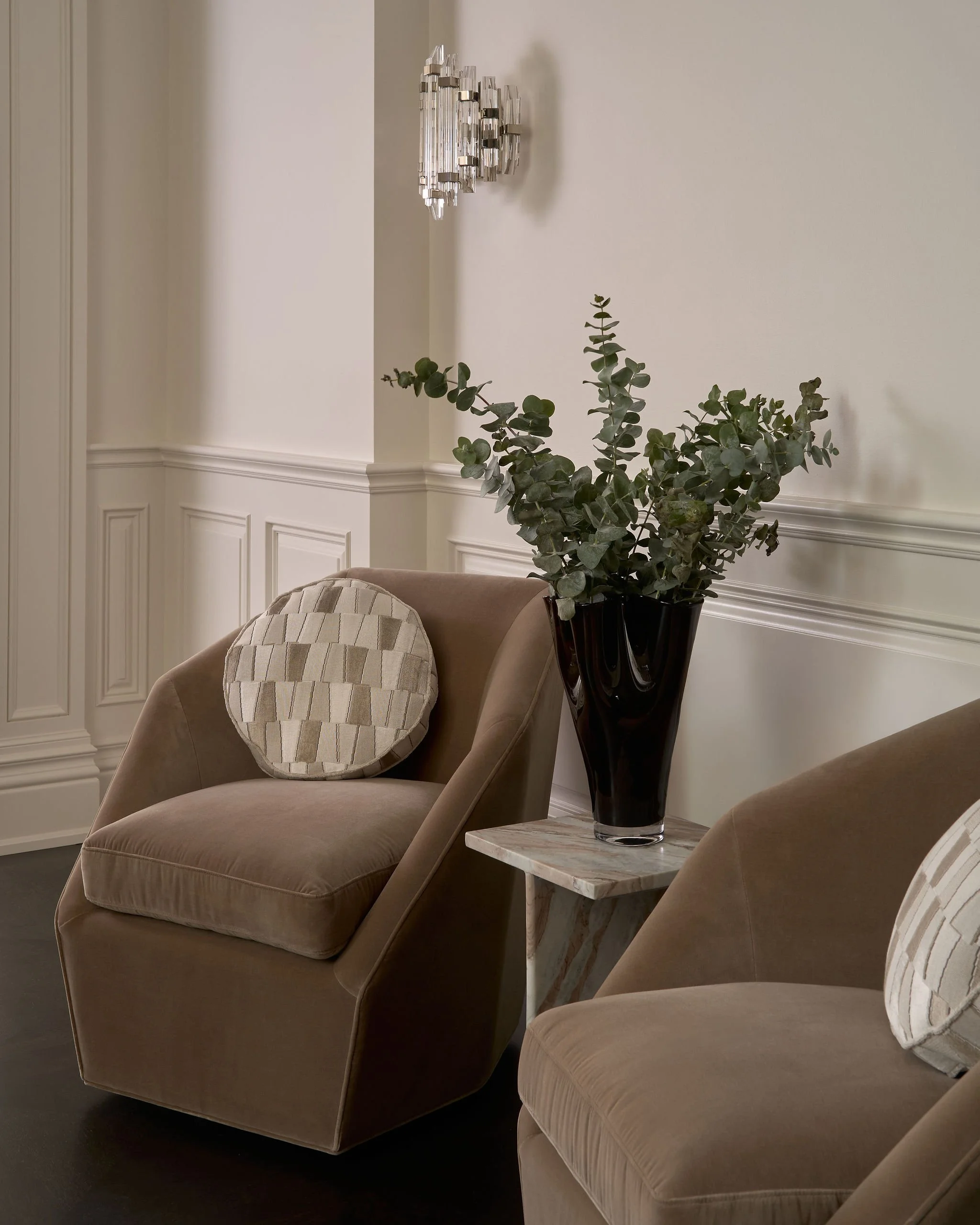 Living room corner with beige armchair, decorative pillow, potted green plant in black vase, and a white marble side table.