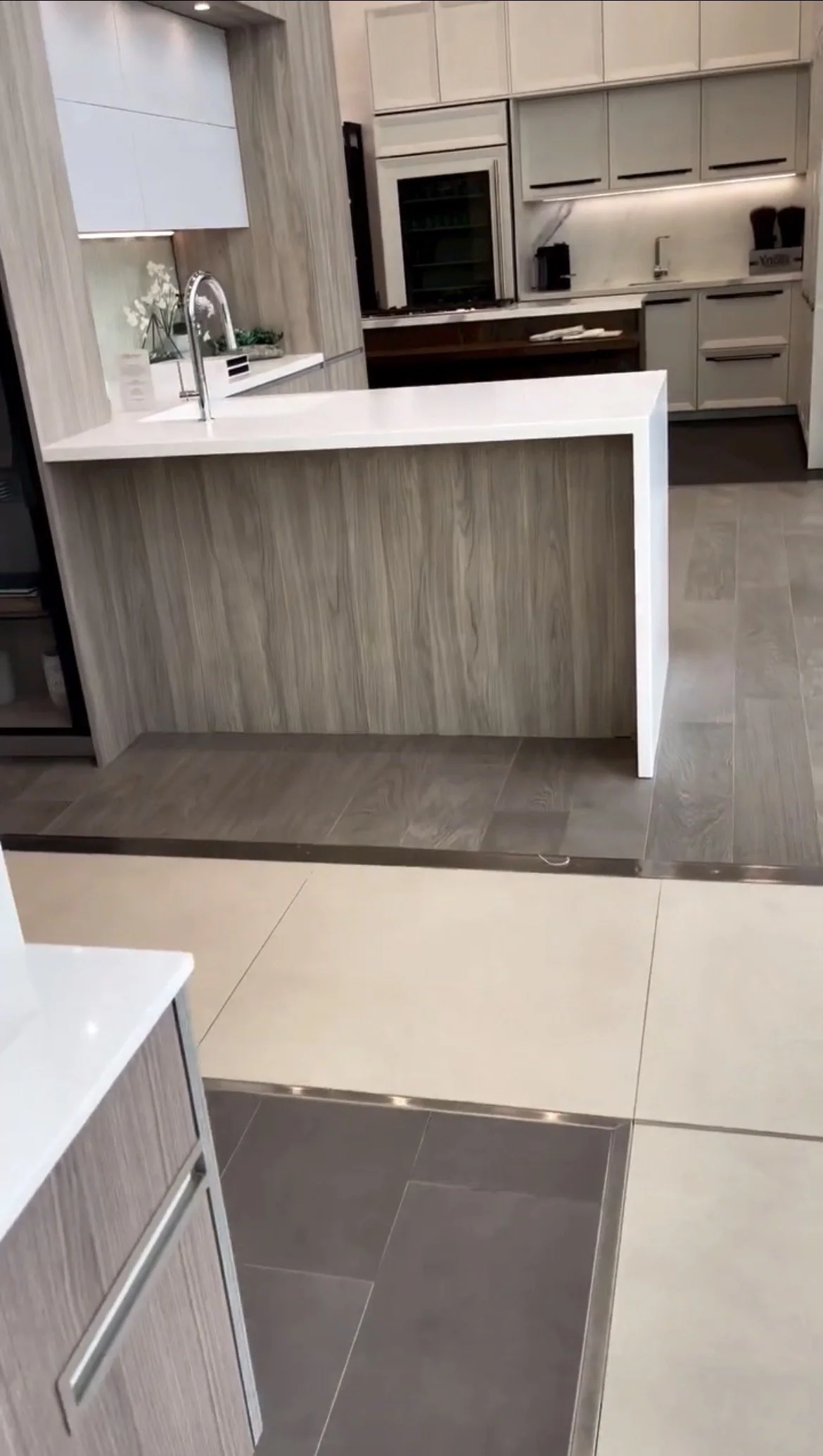 Modern kitchen with a white countertop bar, gray cabinets, a built-in microwave, and a mix of light and dark flooring tiles.