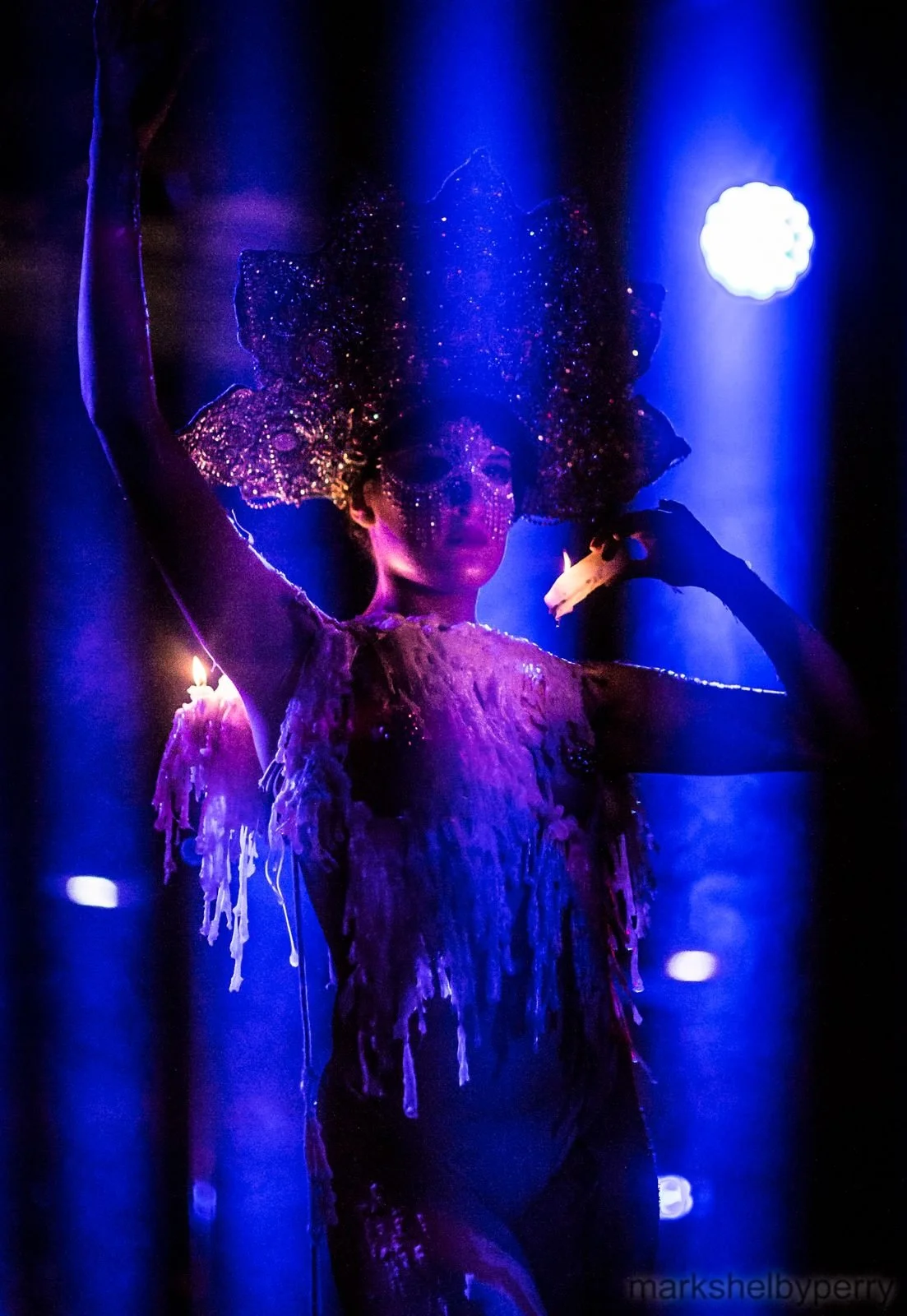 Candle performer in blue stage light. Past Astarte Creative performance.