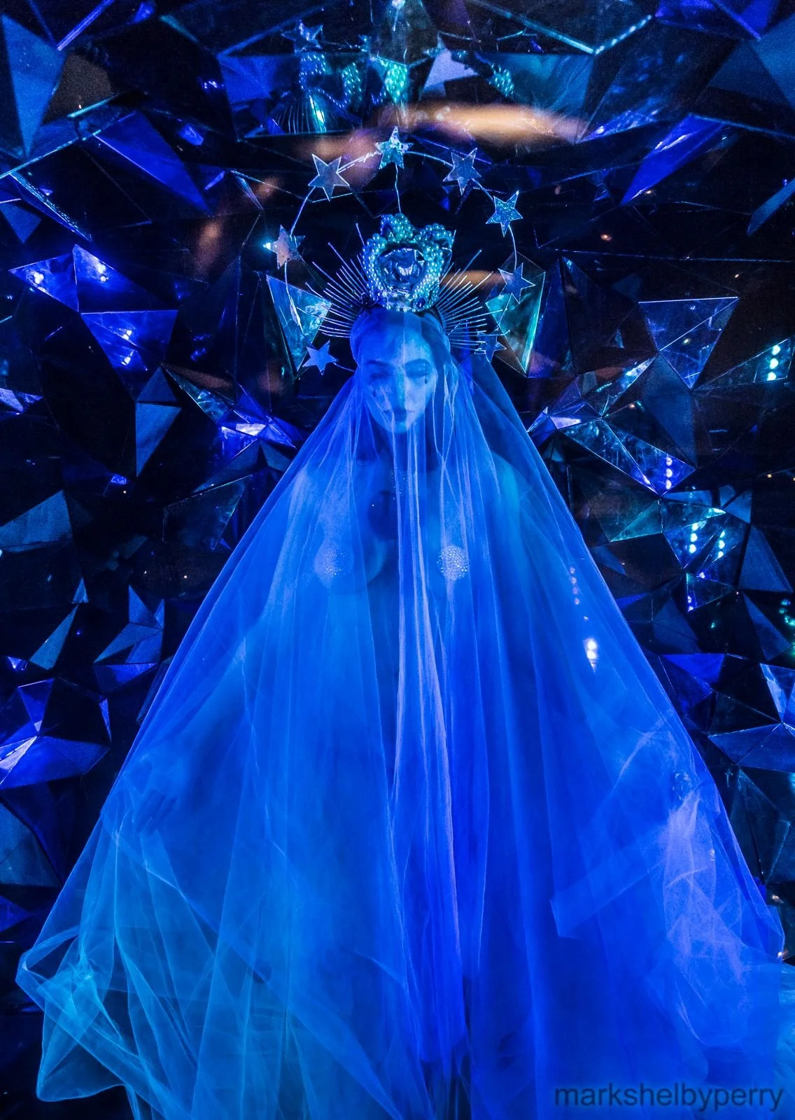 Blue-veiled figure before a mirrored backdrop. Past Astarte Creative performance.