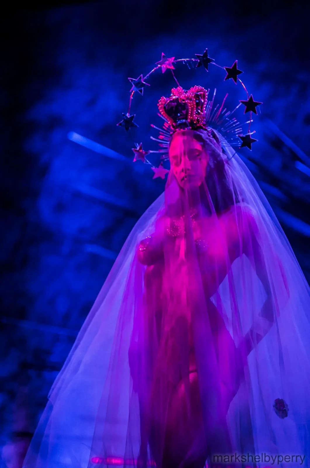 Veiled figure under blue and pink light. Past Astarte Creative performance.