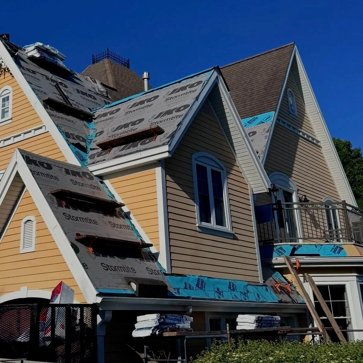 A house under construction with new siding being installed and roofing plywood exposed.