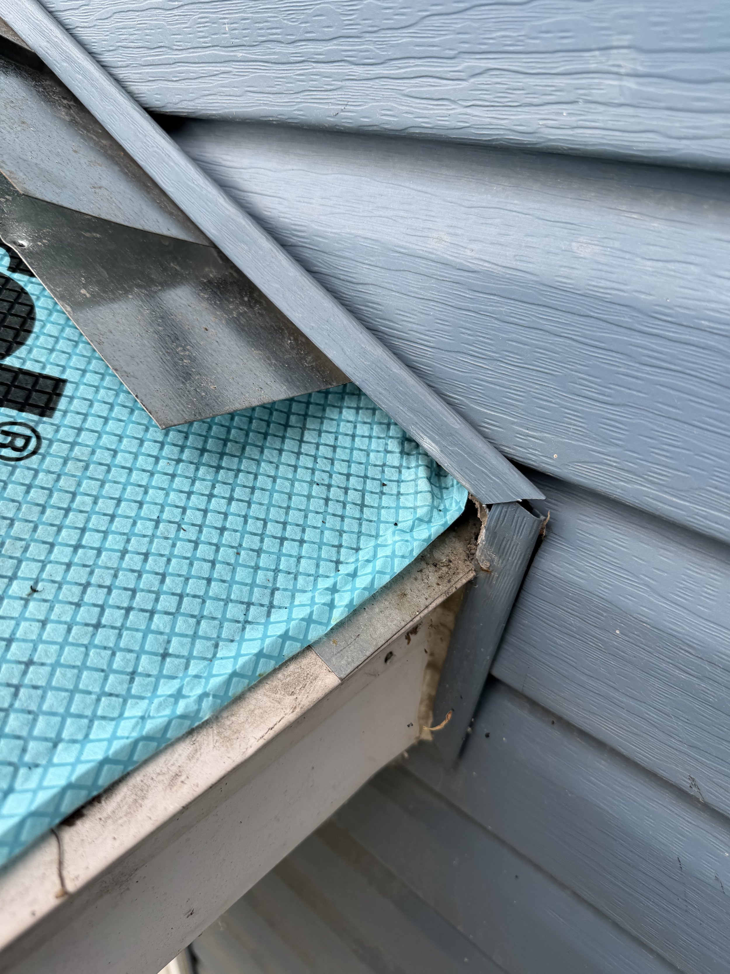 Close-up of a gray plastic window sill and gray siding exterior wall, with a blue textured mat below.