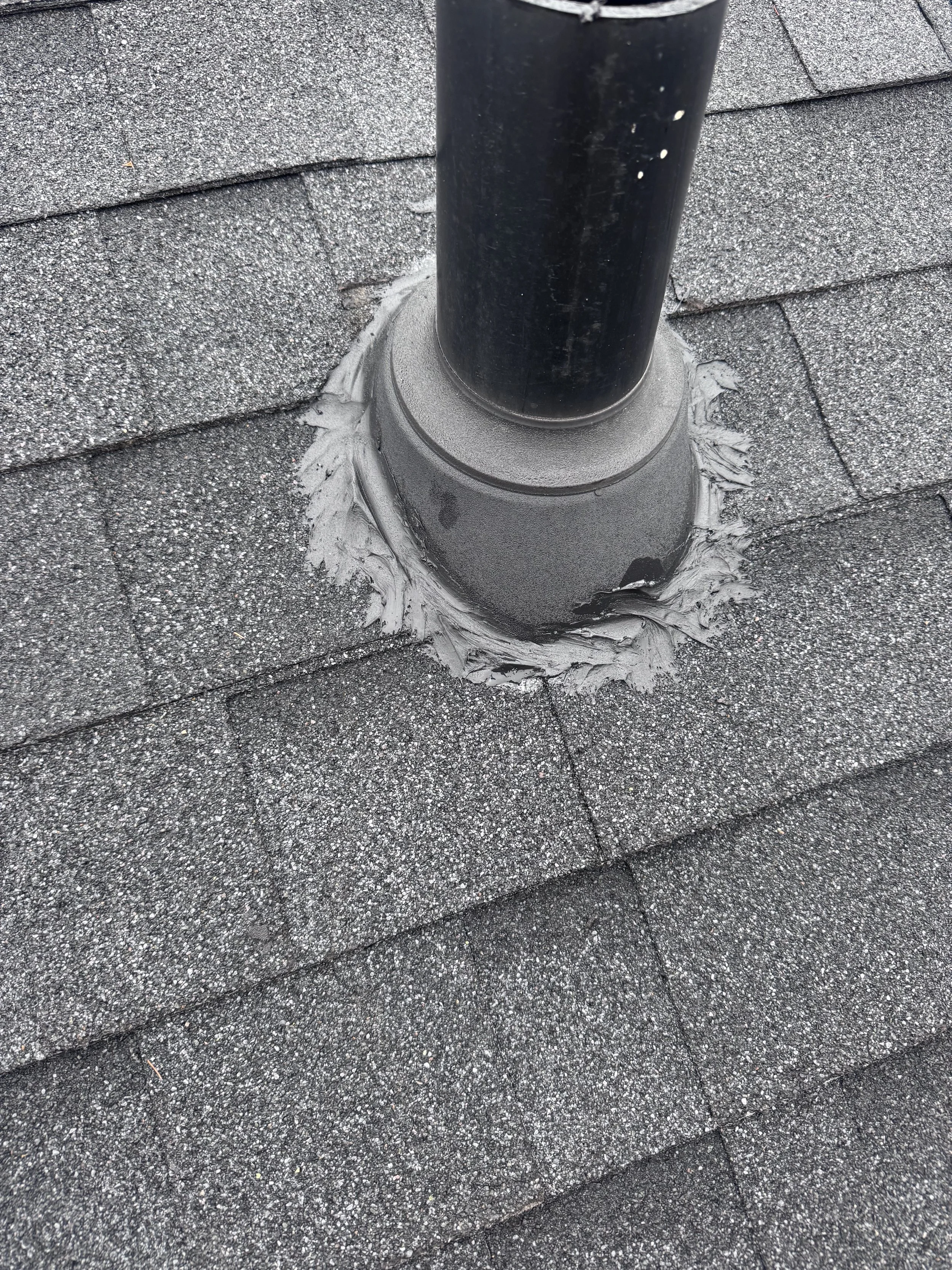 Shingled roof with a black vent pipe and surrounding roofing material.