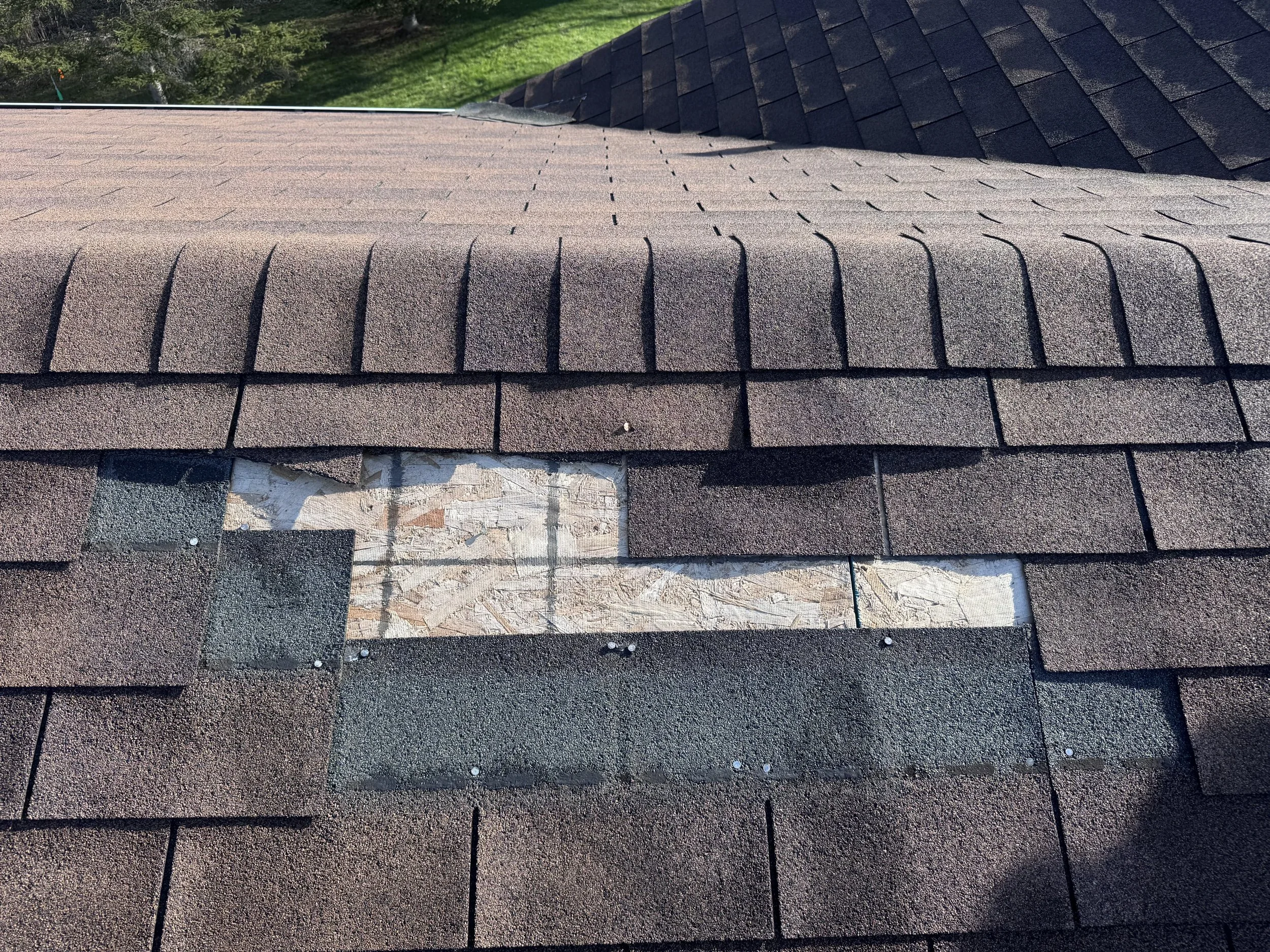 Close-up of a roof with brown asphalt shingles, with some shingles removed near the bottom, exposing the underlying surface.