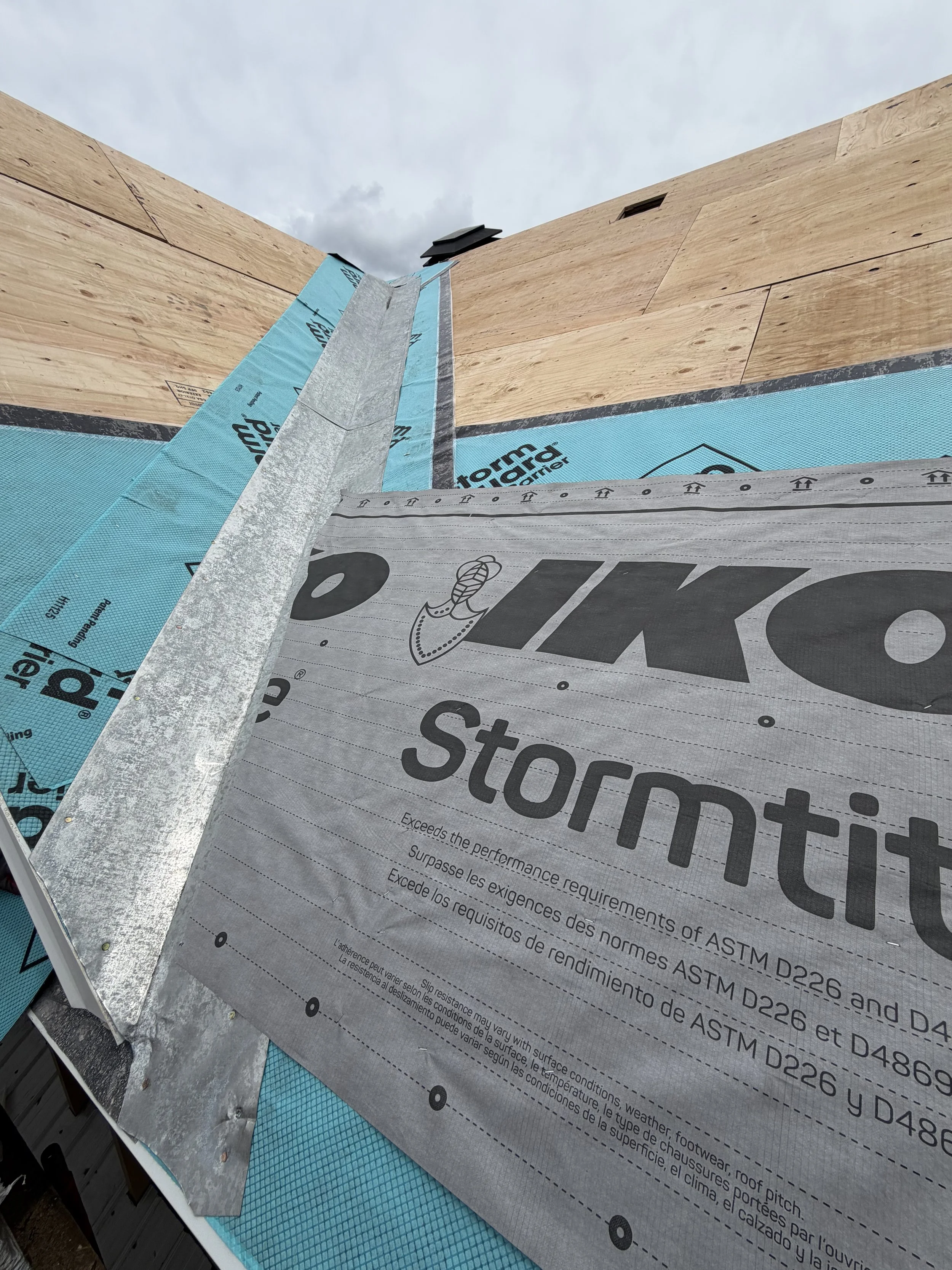 Construction site with roofing materials, including blue weatherproof sheeting and insulation, on a building under construction.