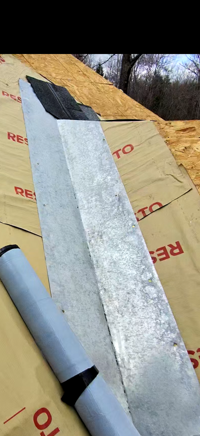 Metal flashing piece on a roof under construction with insulation material and plywood in the background, and trees in the distance.