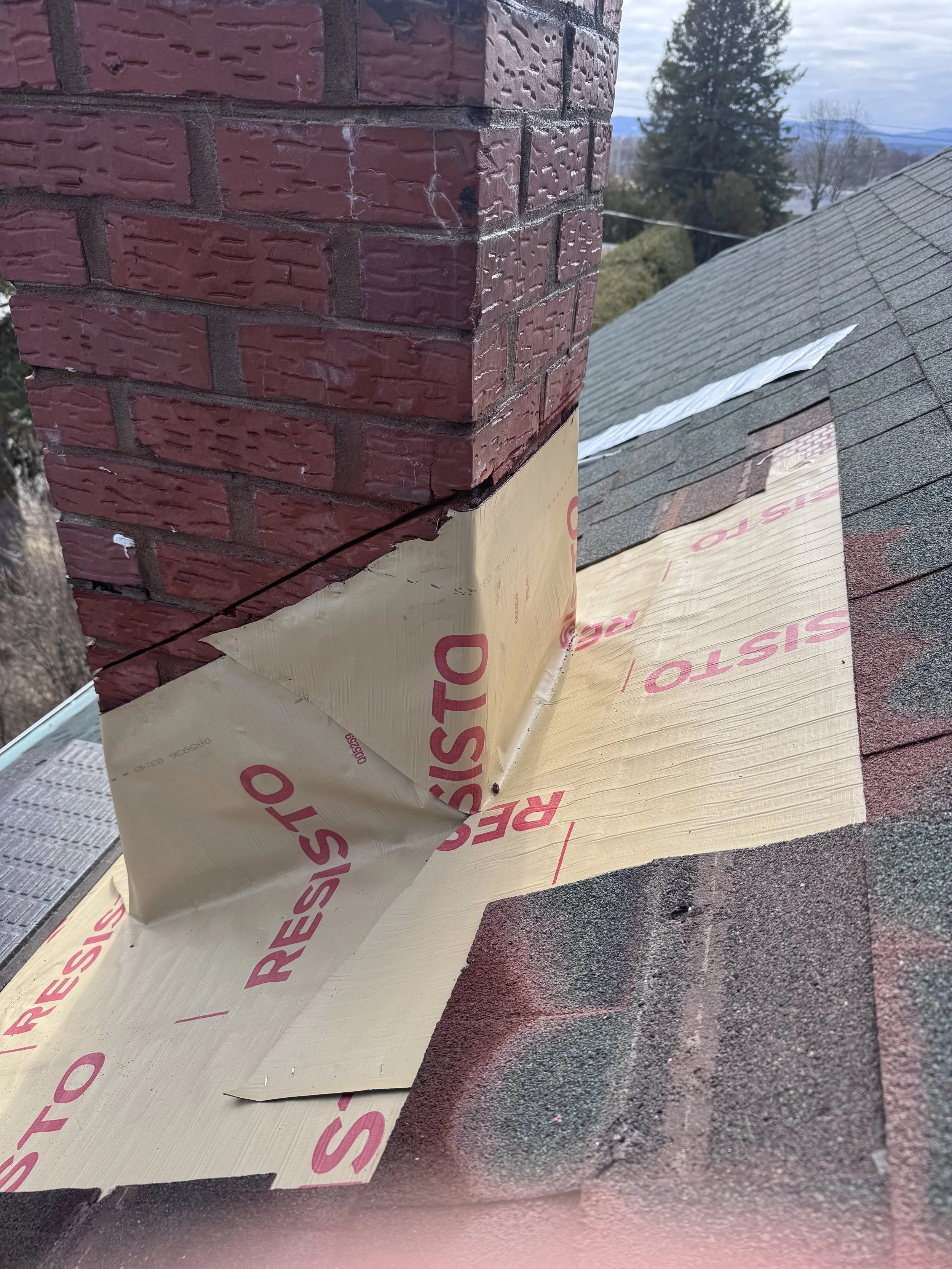 Close-up of a brick chimney with some construction insulation material partially removed, revealing a roofing underlayment beneath.