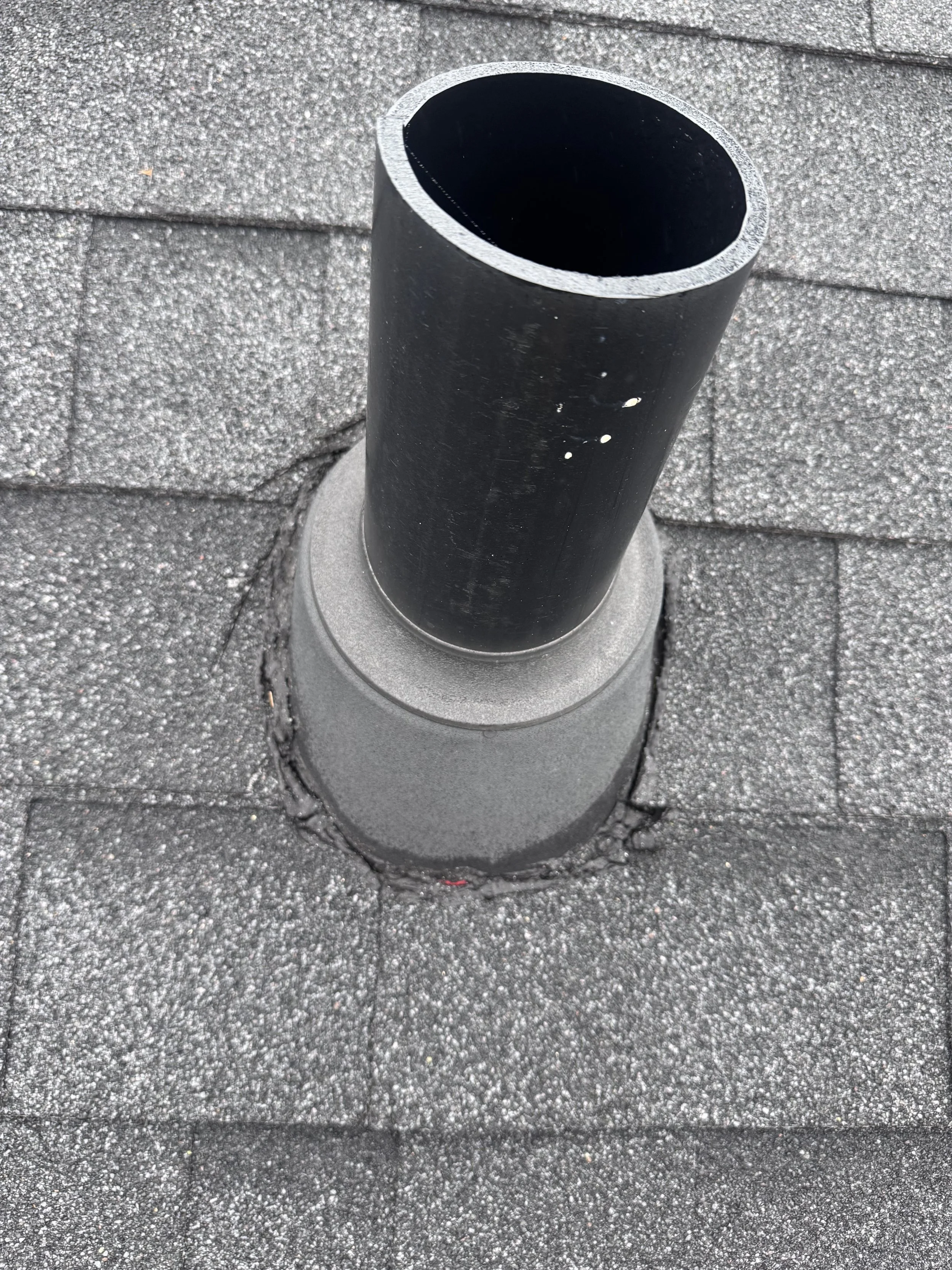 A black cylindrical pipe sticking out of a gray shingled roof.