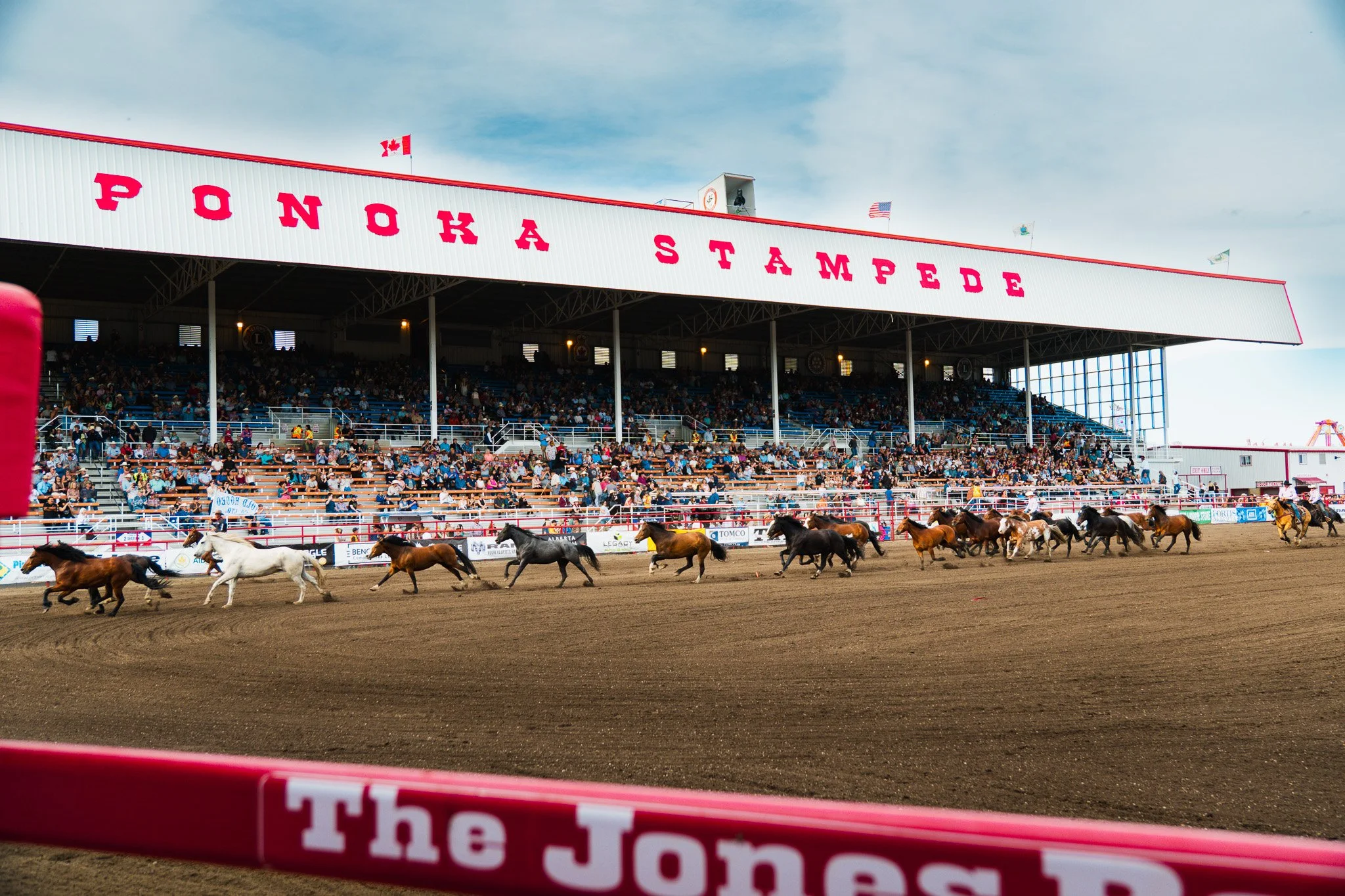 Horse racing at Ponoka Stampede rodeo in Ponoka, Alberta, with a large crowd in the stands and horses on the dirt track.