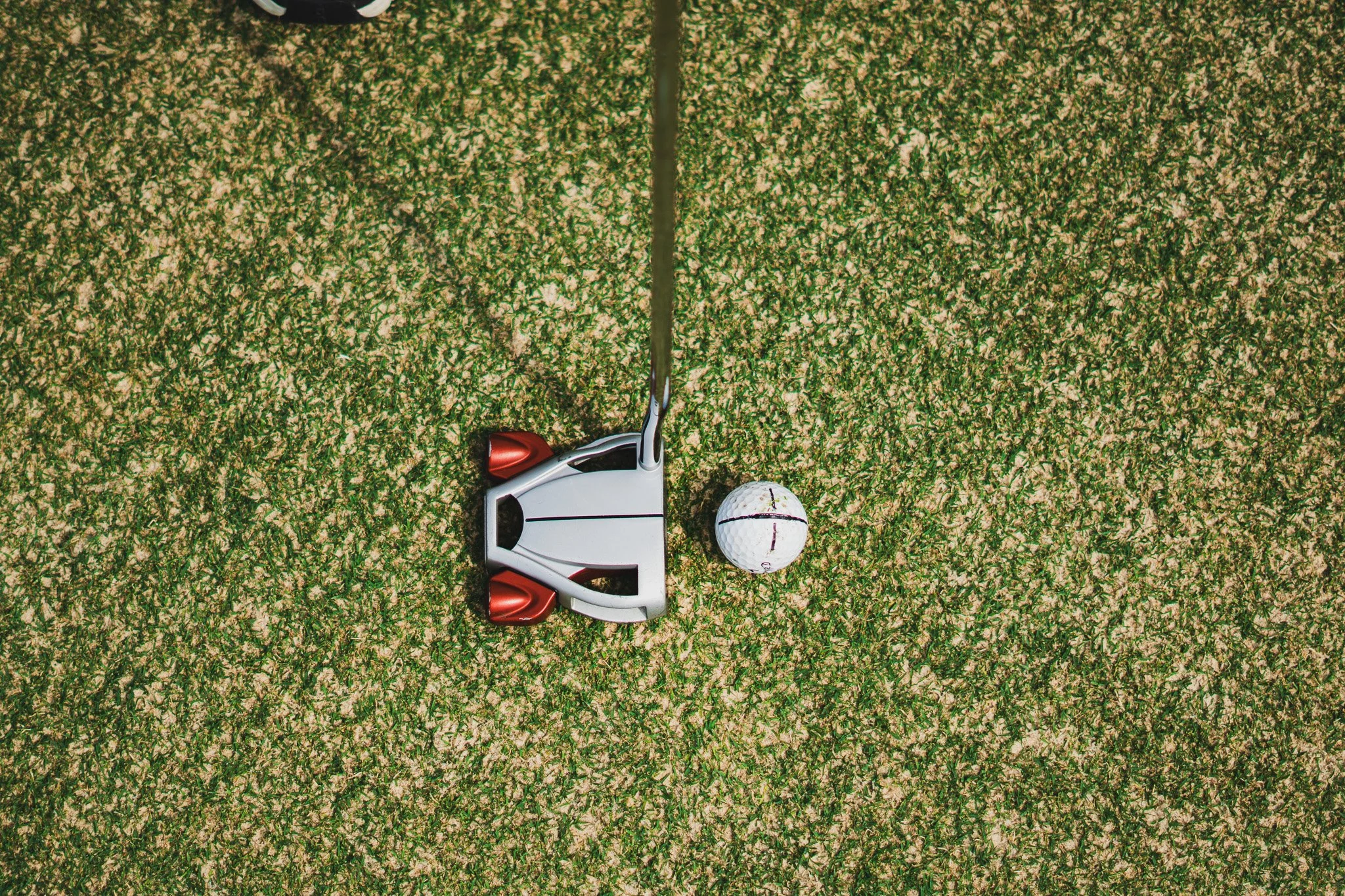Top-down view of a golf course with a golf ball, golf club, and a golf tee placed on grass.