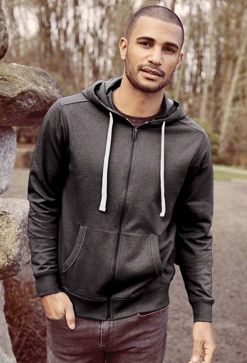 A young man in a black hoodie standing outdoors in a natural setting with trees and rocks in the background.