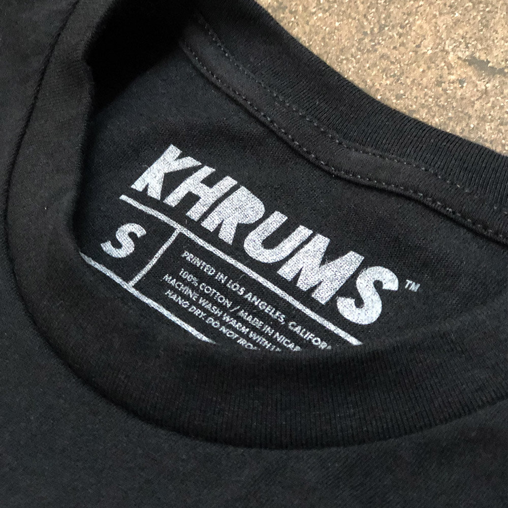 Close-up of a black T-shirt collar label showing the brand 'KHRUMS' and care instructions.