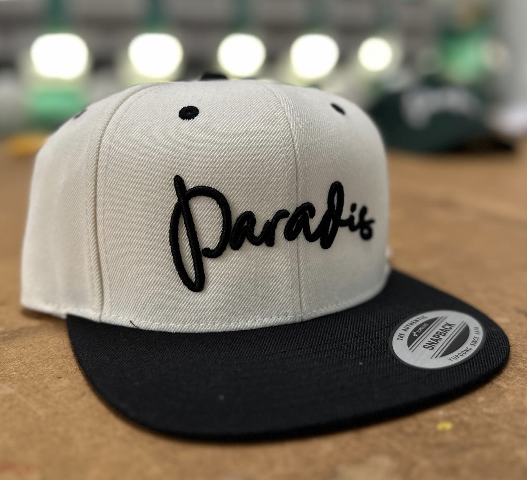 Cap with a black brim, beige crown, and 'Pacros' embroidered in black on the front.