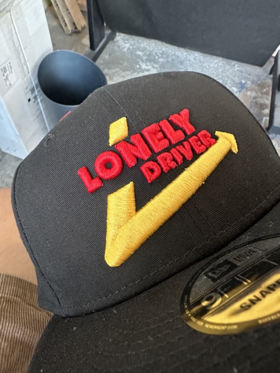 Close-up of a black cap with a yellow checkmark and red embroidered text saying 'Love My Delivery'.