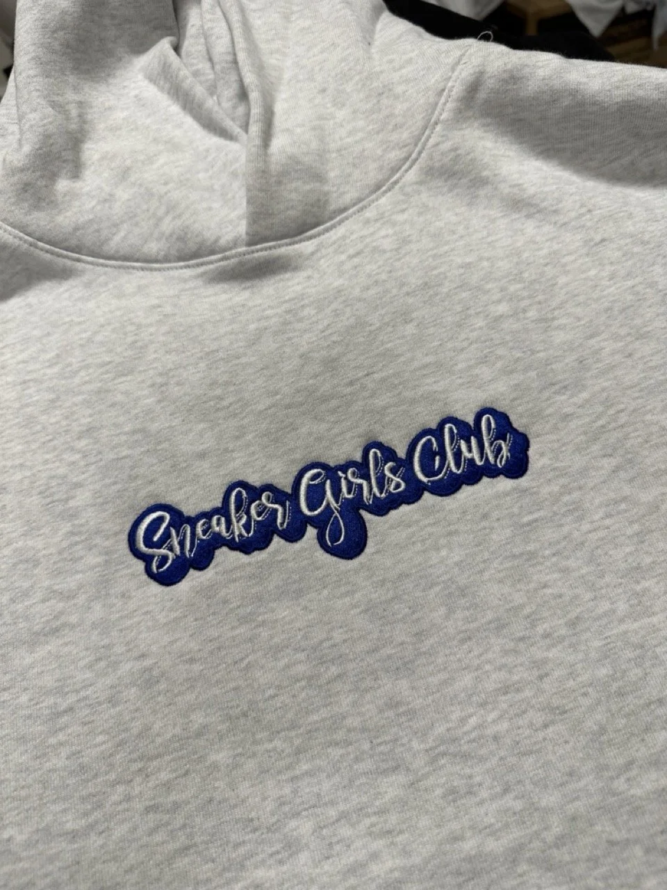 Gray sweatshirt with embroidery that reads 'Sneaker Girls Club' in blue and white thread.