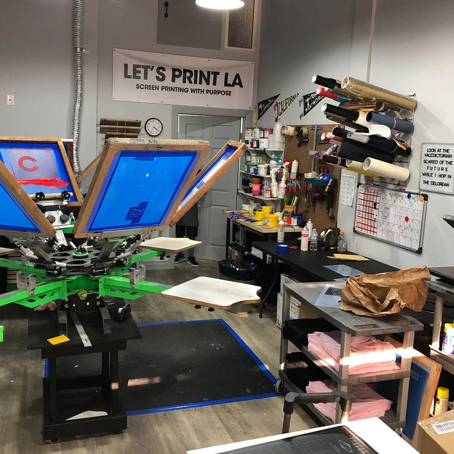 A screen printing workshop with printing presses, rolls of film, and various supplies and tools for screen printing.