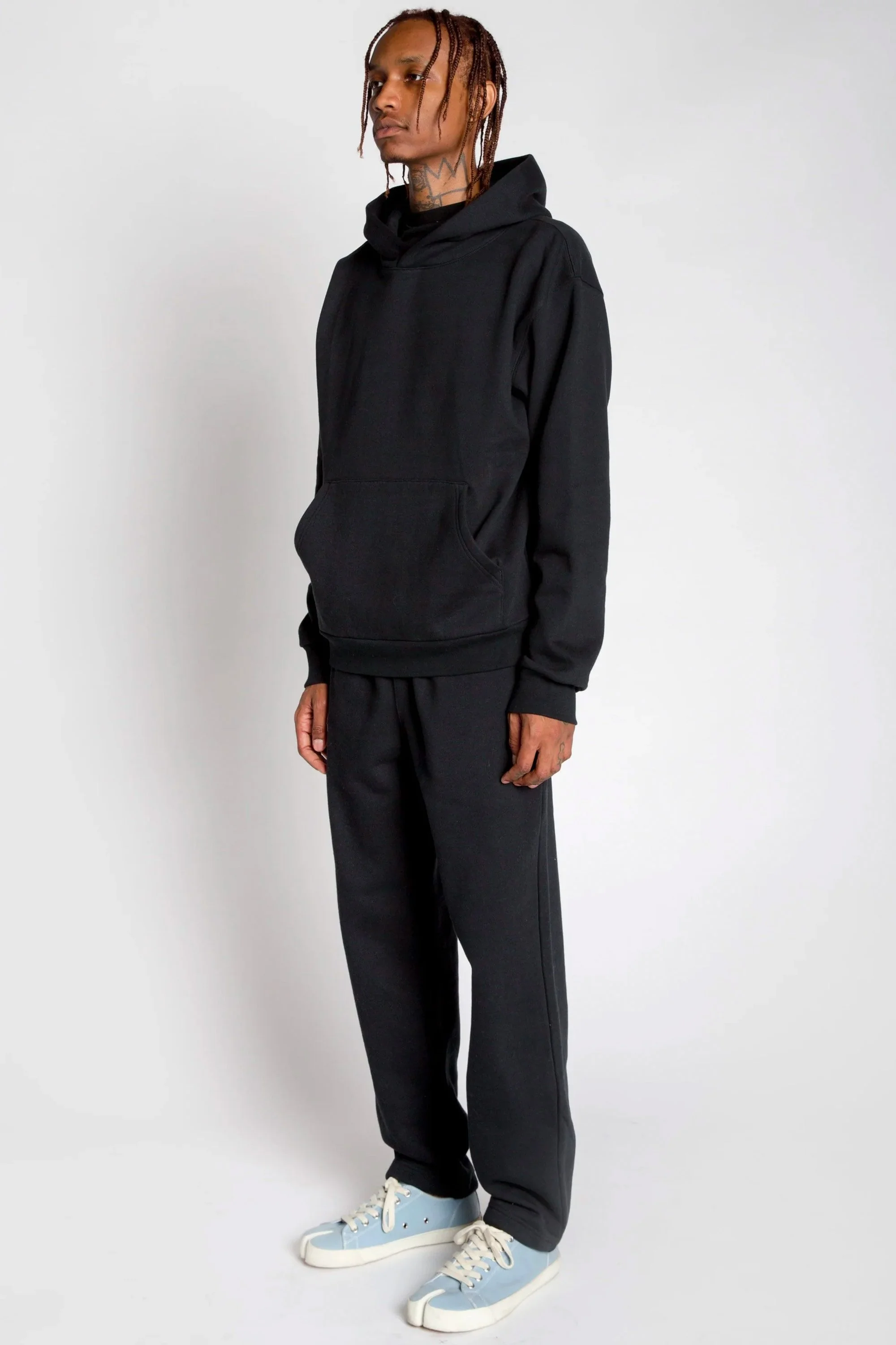 Person in black hoodie and sweatpants wearing light blue sneakers standing against plain white background.