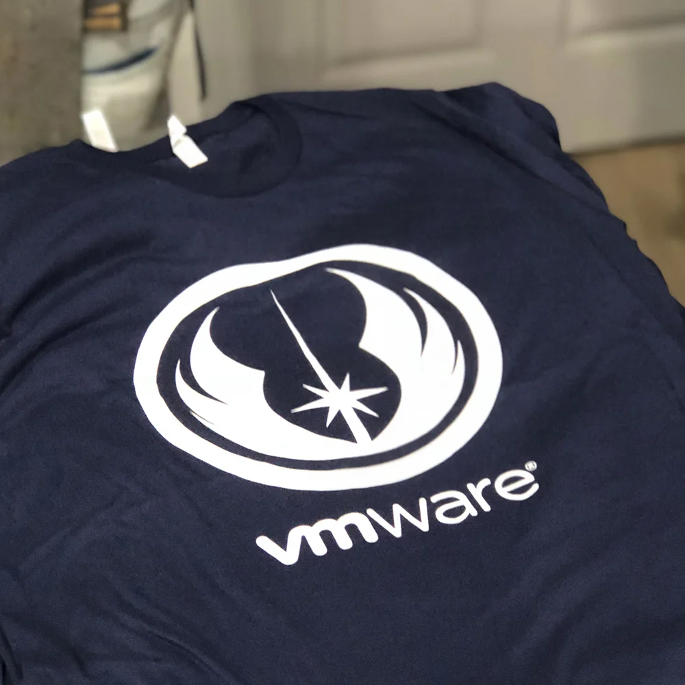 A navy blue t-shirt with the VMware logo, which features a stylized star and orbit design, laid flat on a surface.