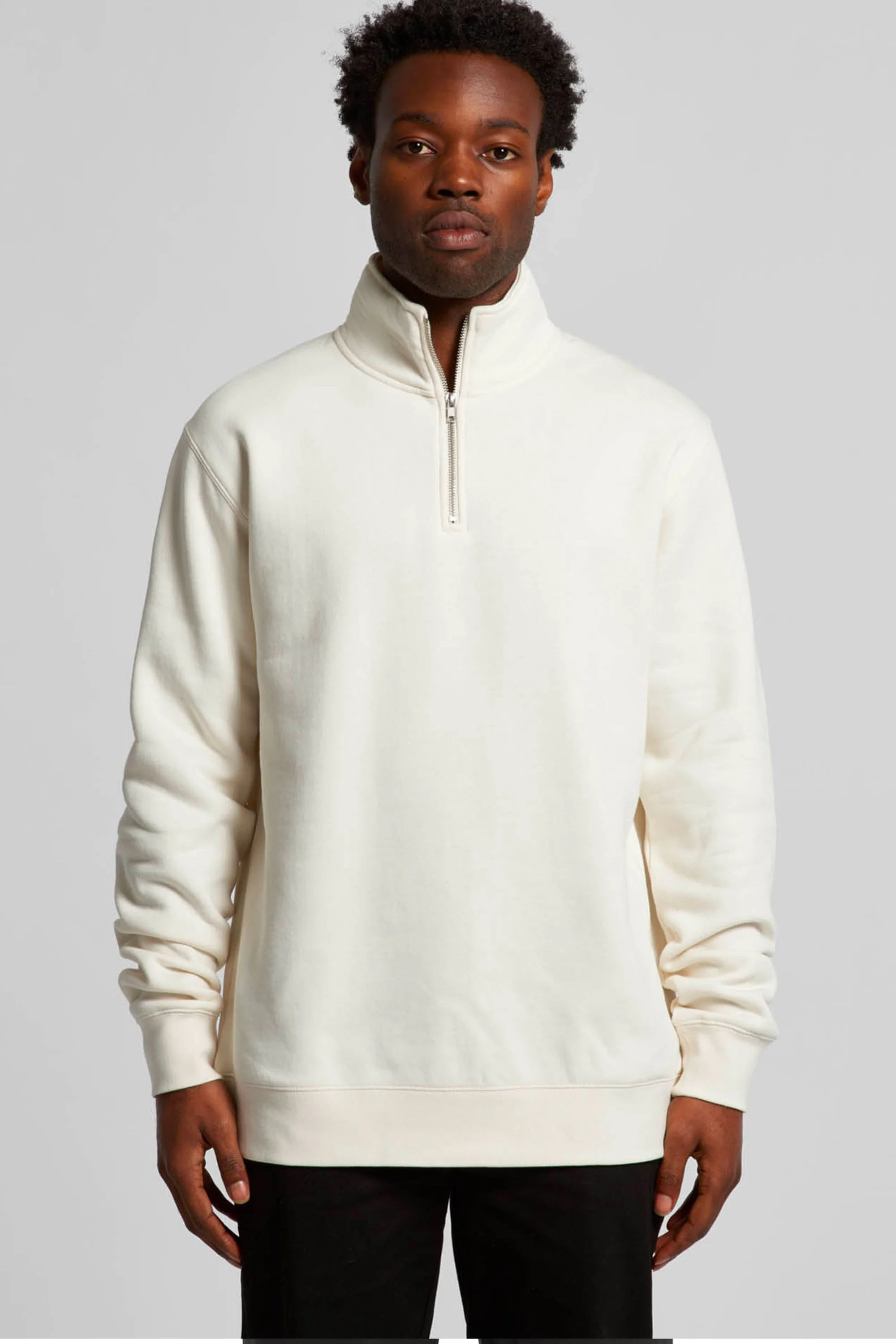 A man wearing a cream-colored quarter-zip pullover with a stand-up collar, standing against a plain light gray background.