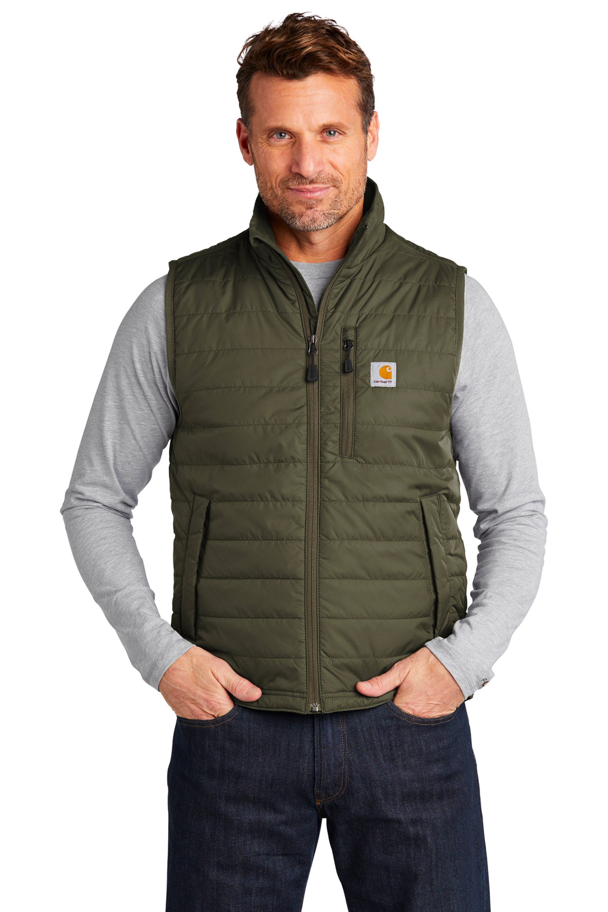 A man with brown hair and blue eyes wearing a gray long-sleeve shirt and a green puffer vest with a Carhartt logo, standing with hands in his pockets against a plain white background.