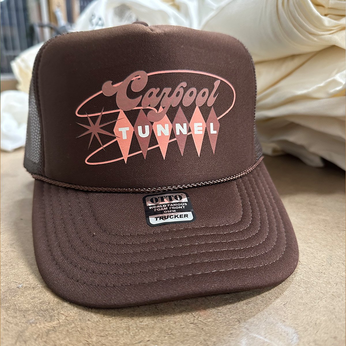 A brown trucker cap with a vintage design featuring the text 'Carpool Tunnel' and geometric starburst graphics.