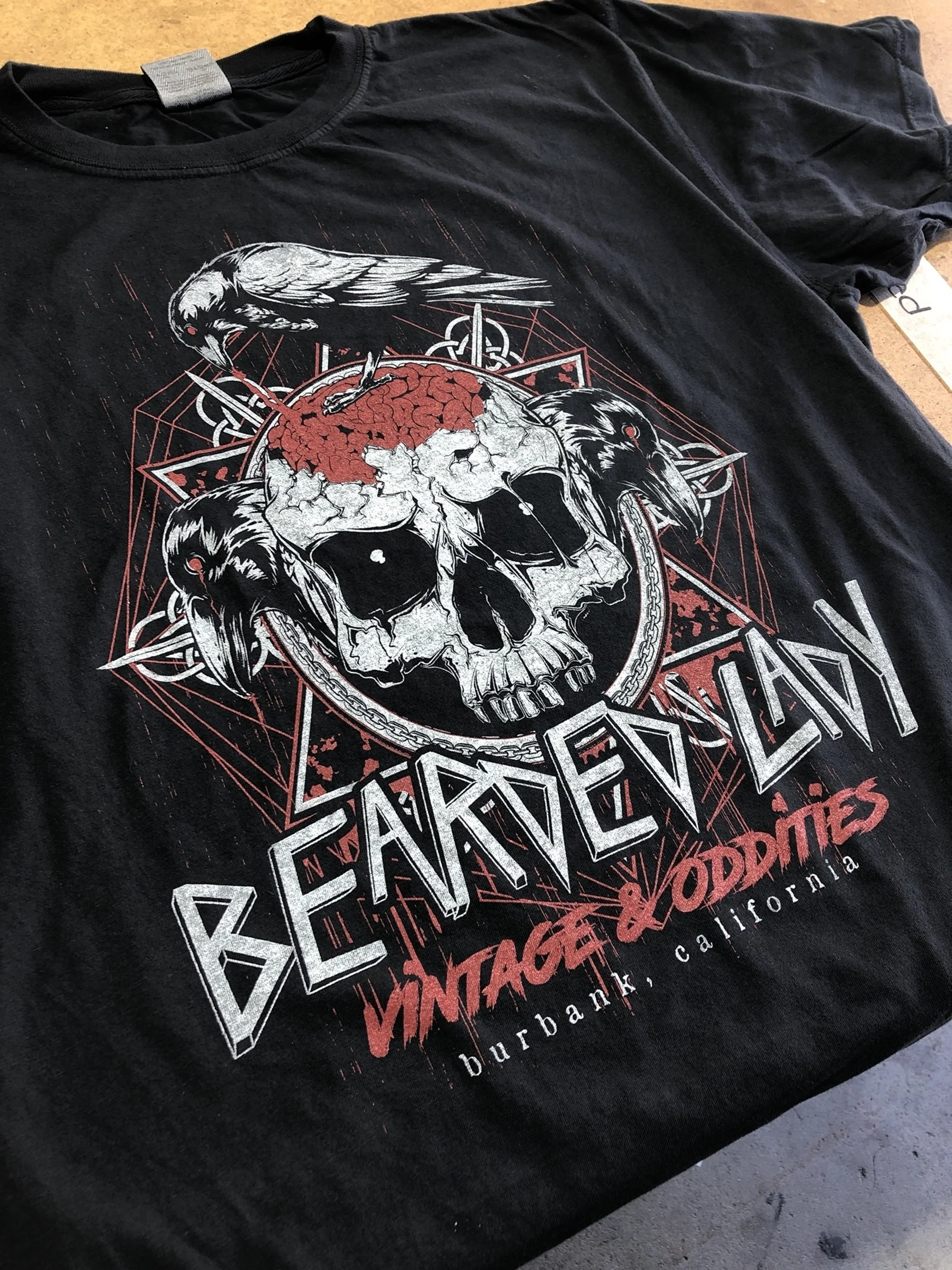 Black T-shirt with a graphic of a skull with a brain on top, surrounded by a raven, geometric patterns, and text that reads 'BEARDED' and 'VINTAGE & ODDITIES', highlighting Burbank, California.