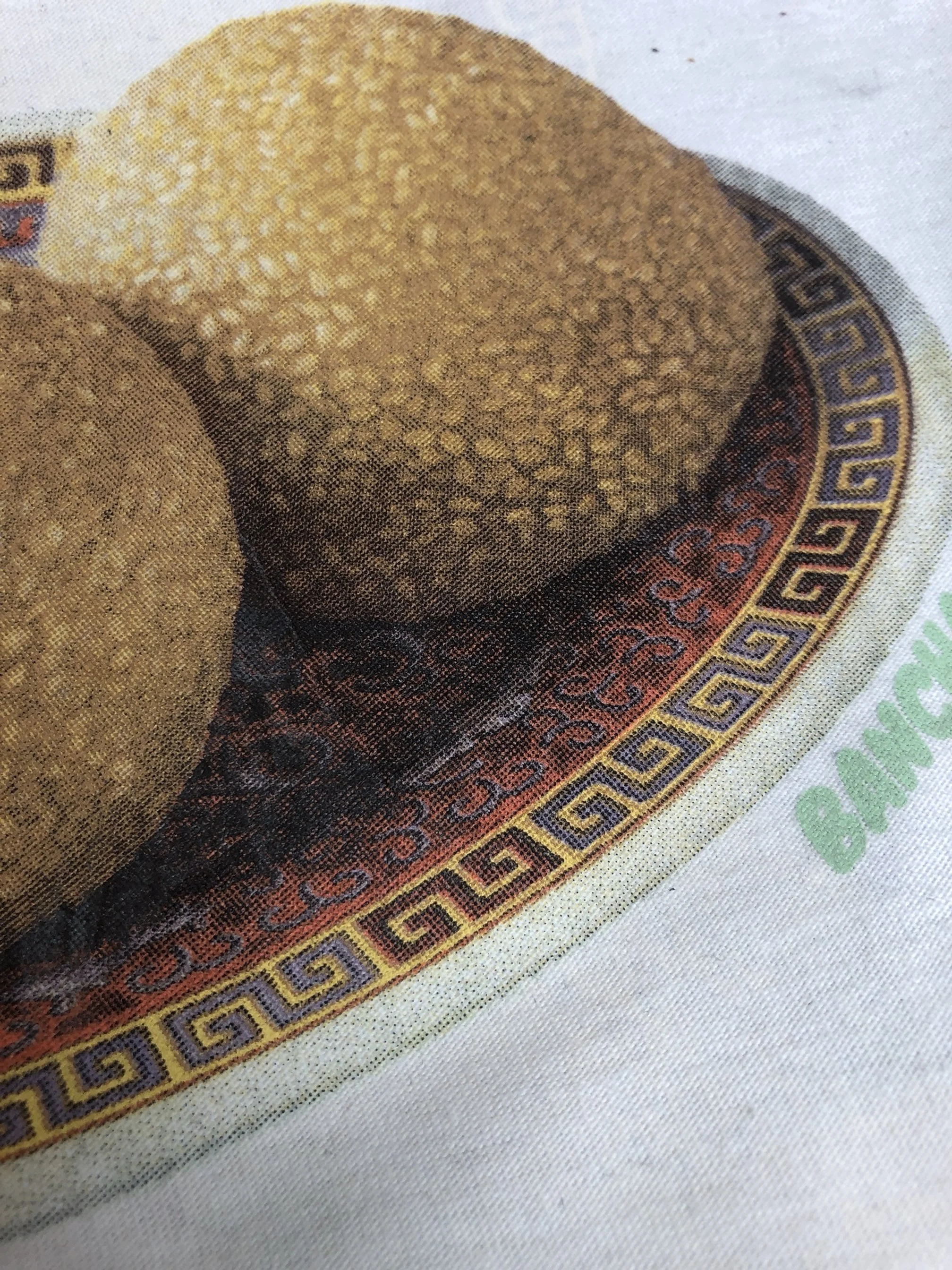 Close-up of a Thai banknote featuring a rounded, textured object, possibly a fruit, with intricate decorative patterns including Greek key motifs around the border.