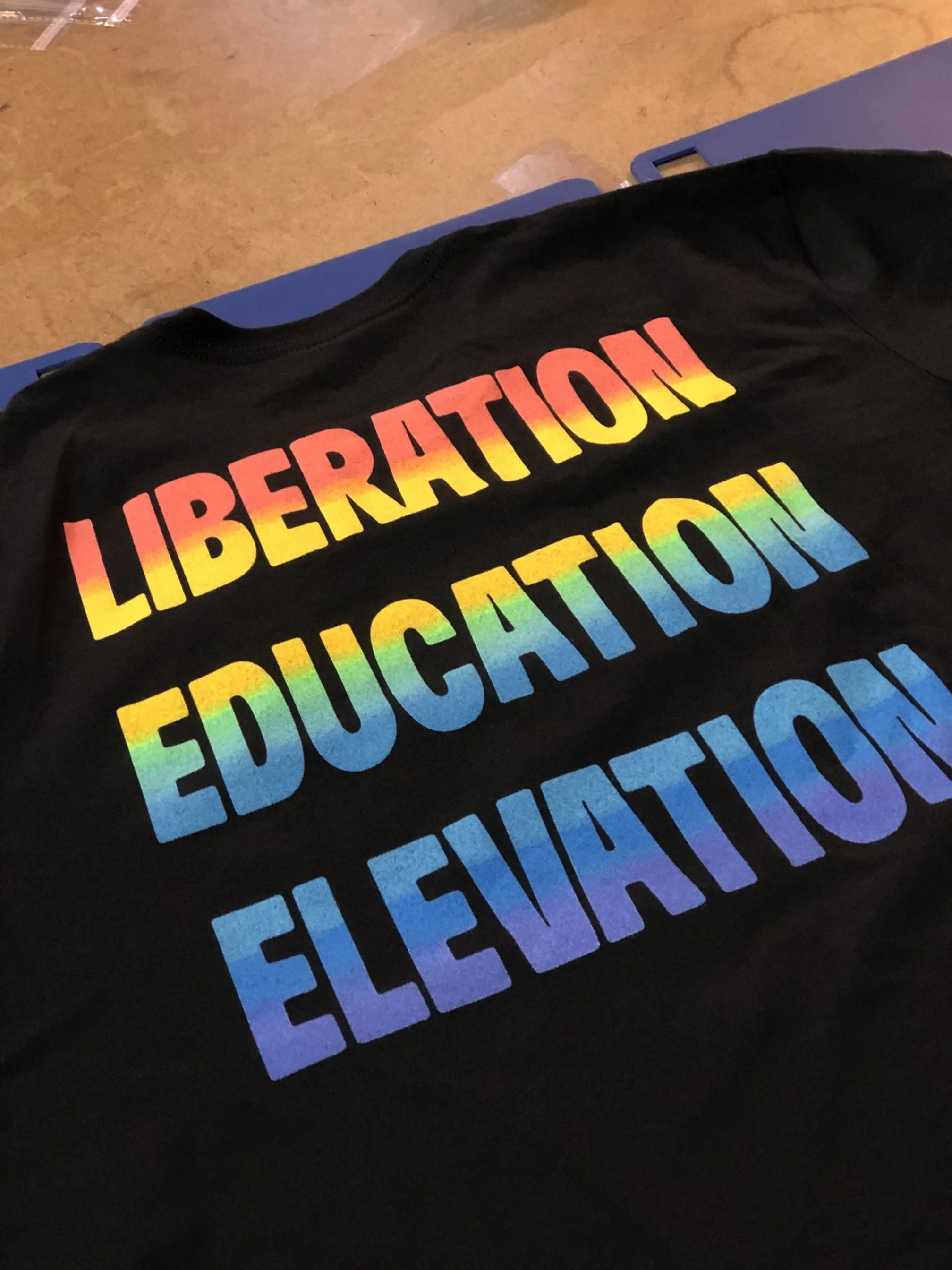 Black T-shirt with rainbow-colored text reading 'LIBERATION,' 'EDUCATION,' and 'EQUALITY'