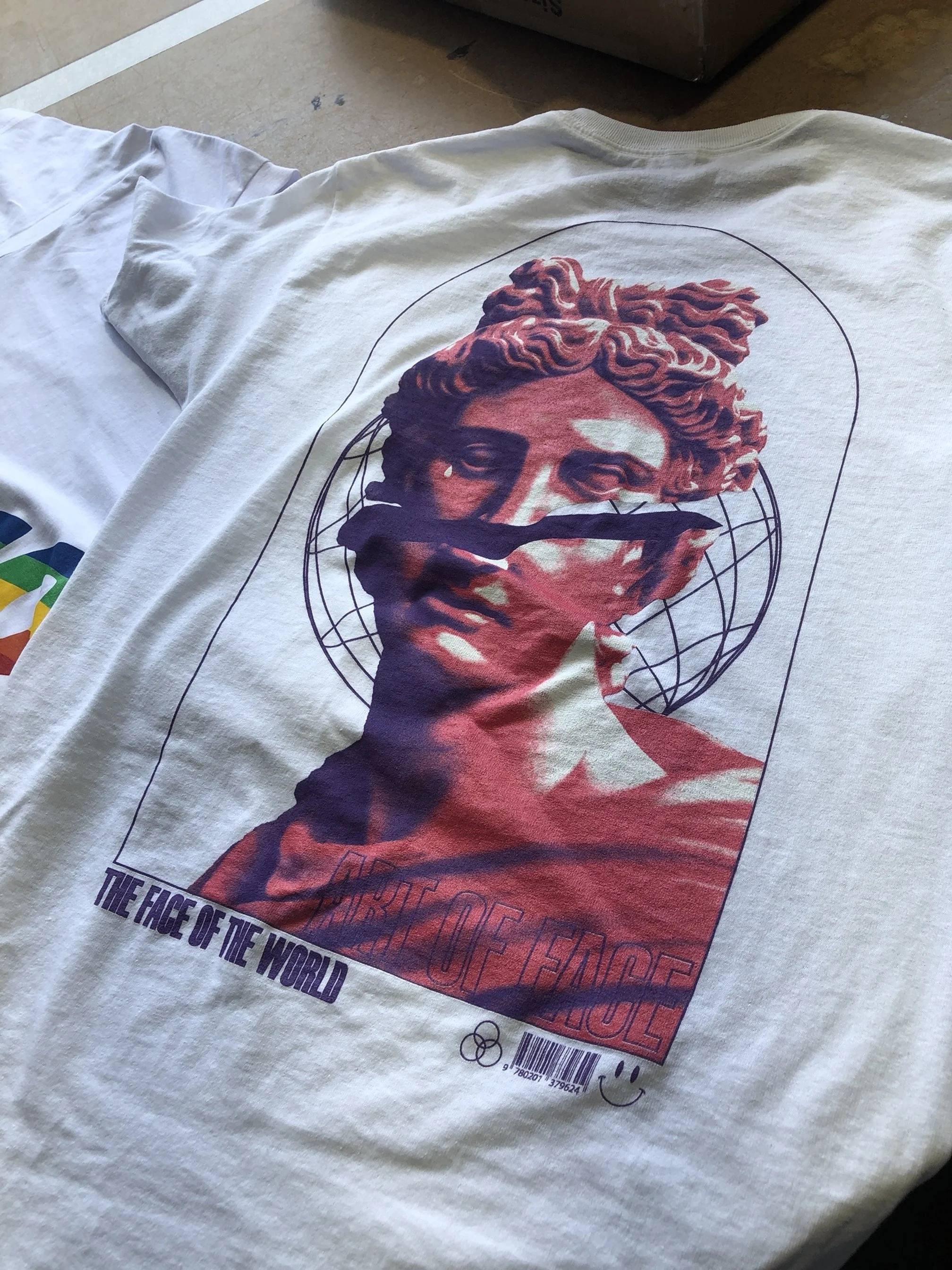 White T-shirt with a graphic of a classical statue's head, surrounded by a globe outline, with the text 'The Face of the World' underneath.
