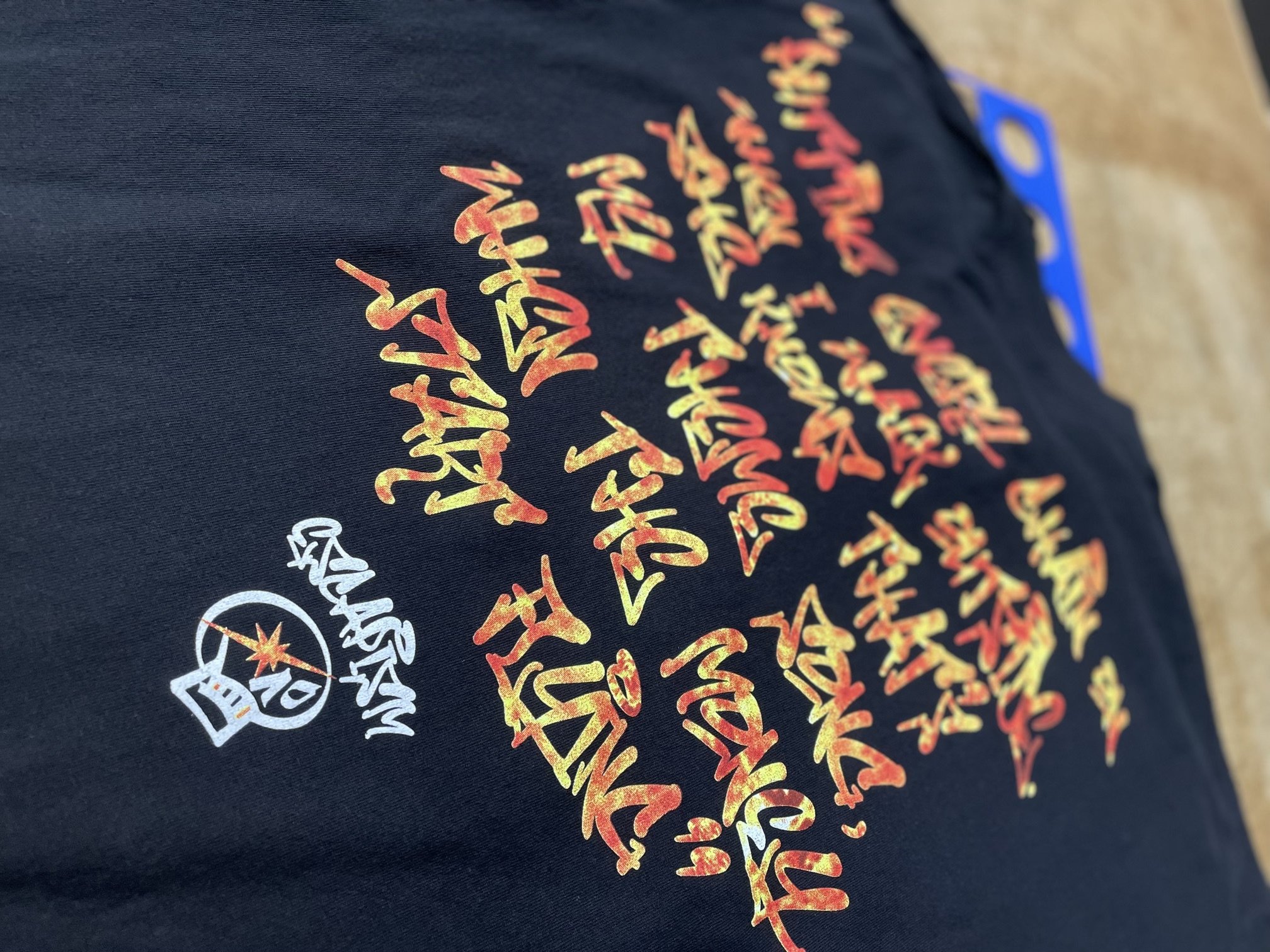 A black piece of clothing with red, yellow, and orange stylized text and a white logo featuring a star on a dark background.