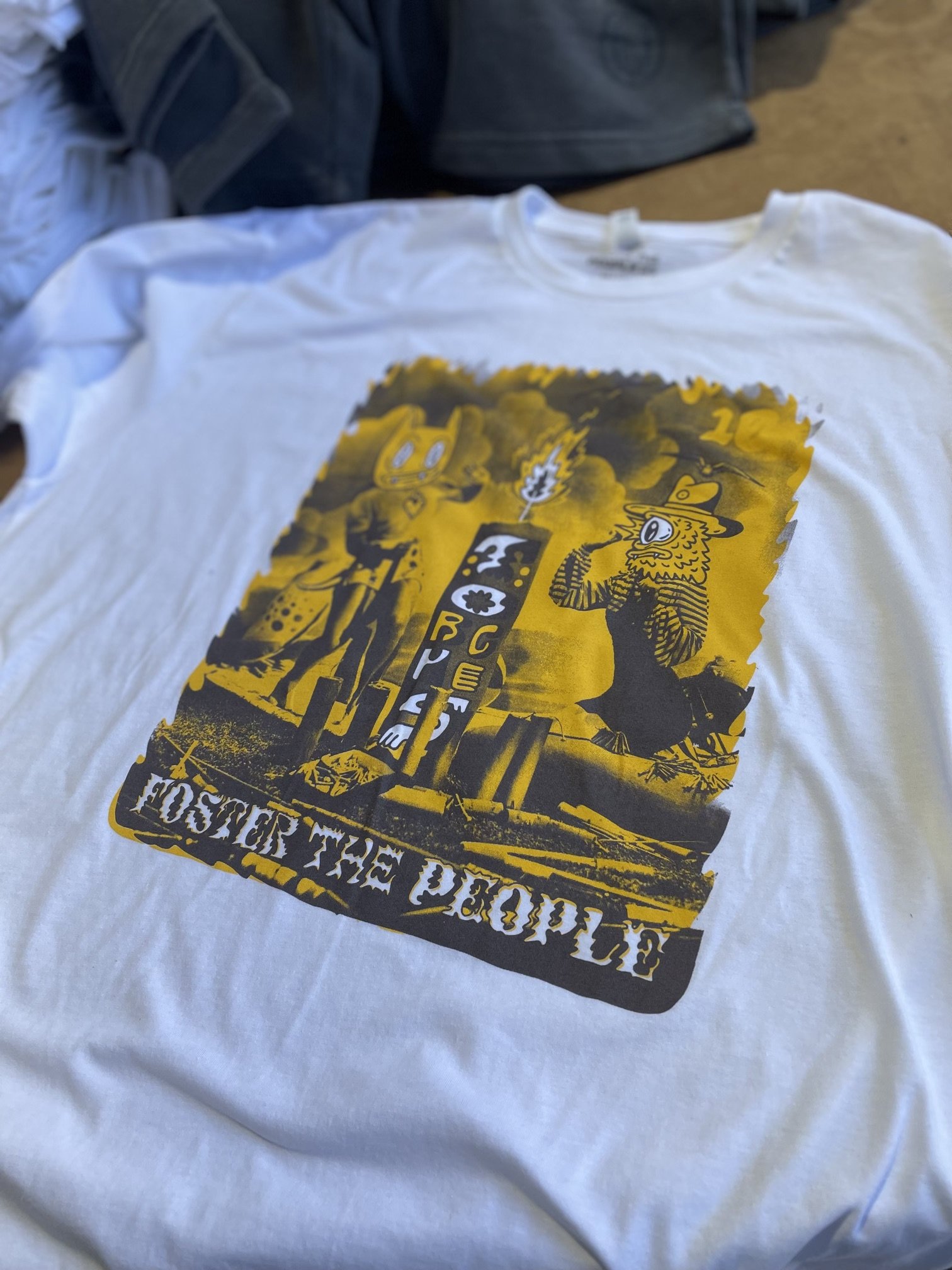 White T-shirt with a yellow and black graphic design featuring cartoon characters and a street scene, with the text "HOSTER THE PEOPLE".
