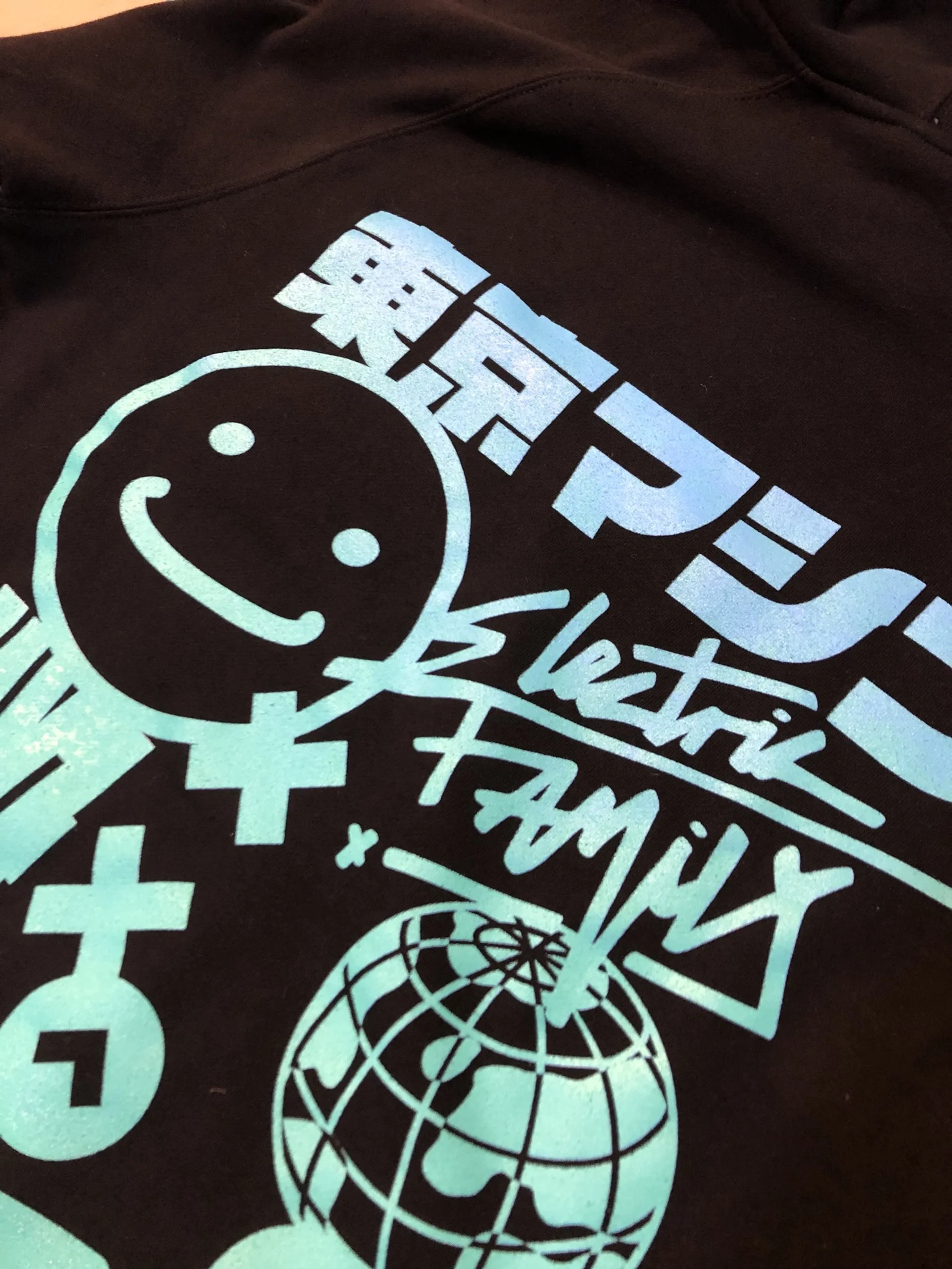 Close-up of a black t-shirt with a colorful graphic design including a smiley face, text, and globe imagery.