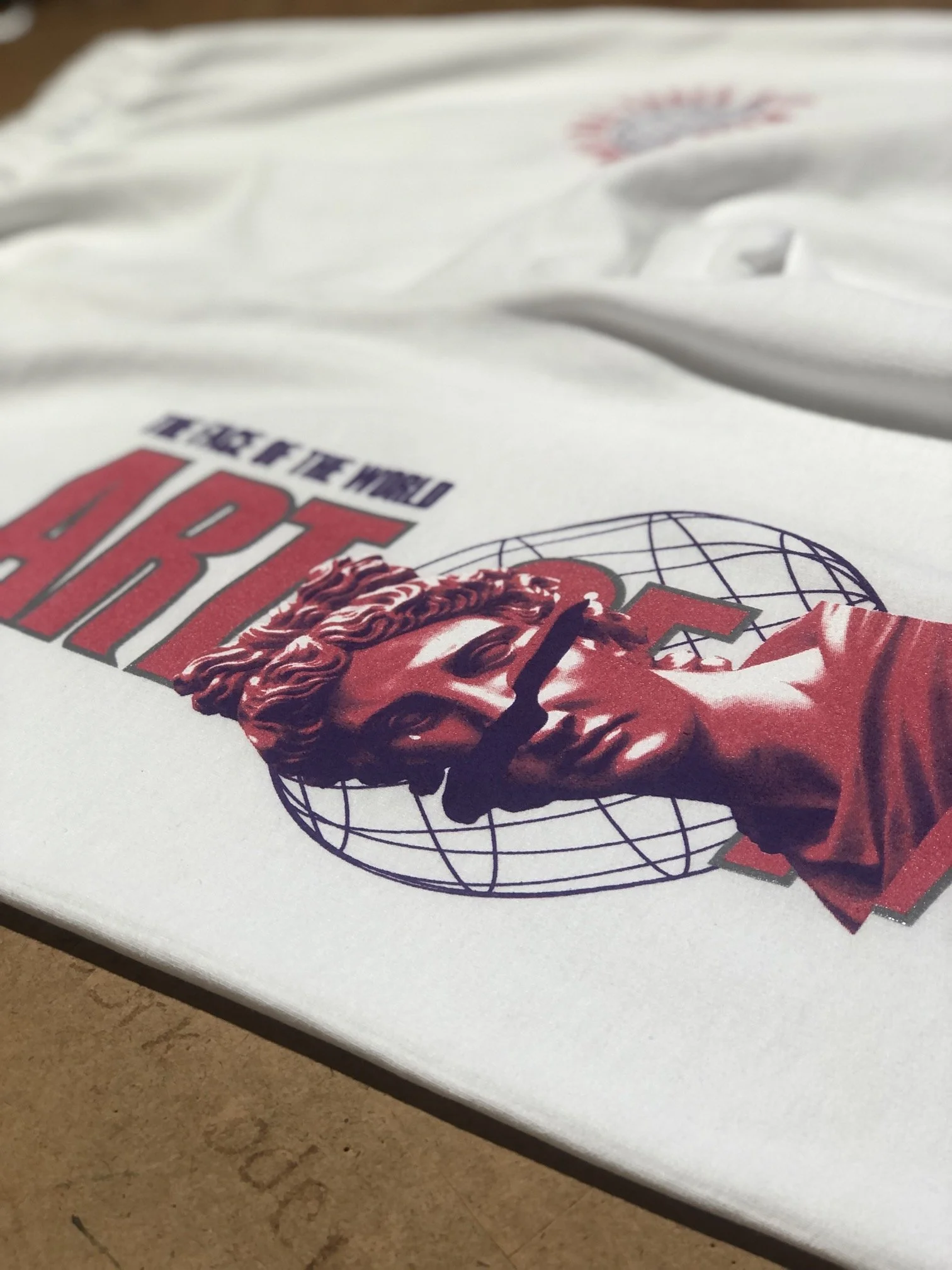 Close-up of a white t-shirt with a graphic design featuring a classical bust and a globe, with text that says 'THE TRUE HERO'.