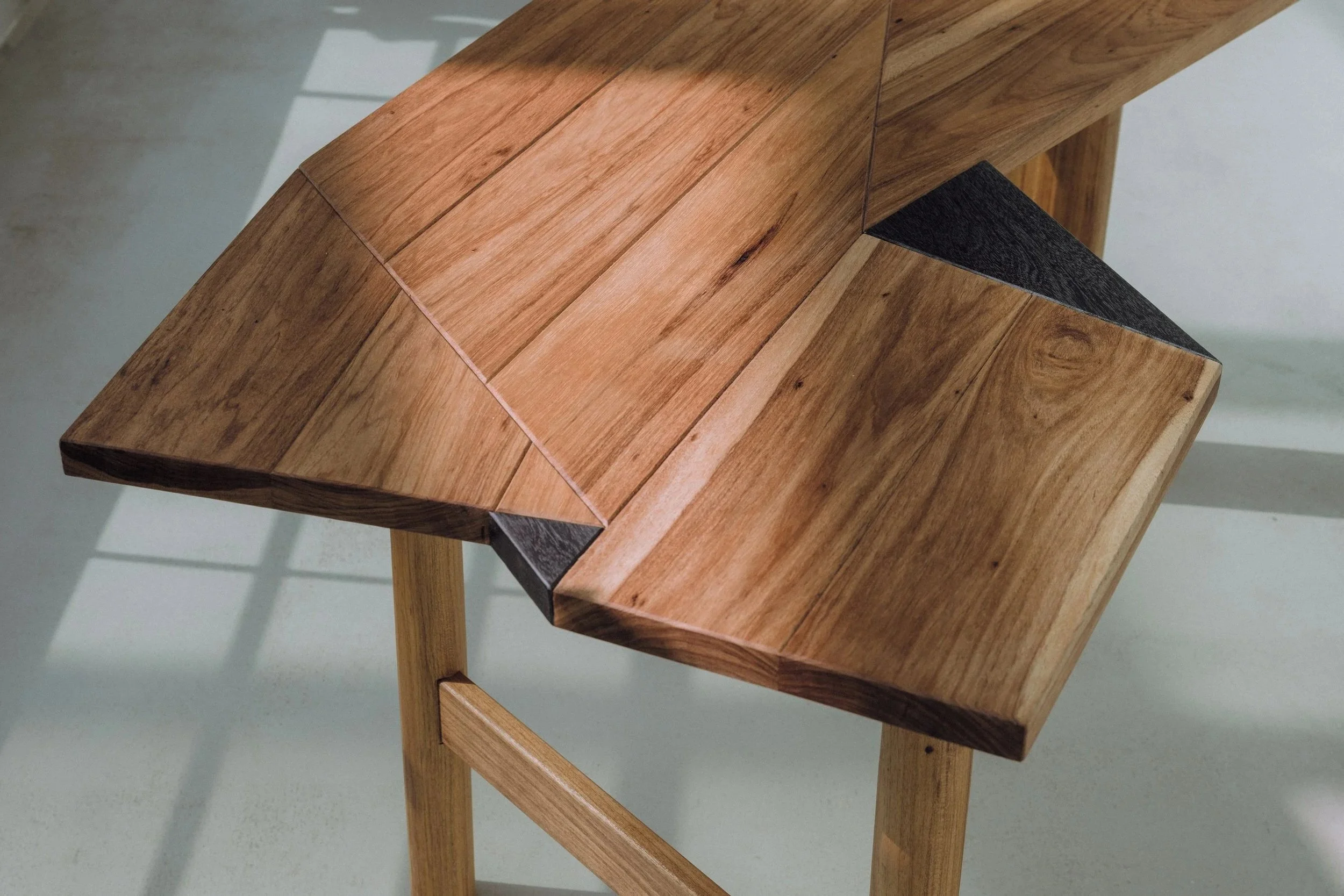 Bureau design en bois massif avec un jeu de couleur et de veinage, supporté par des pieds dont les formes contrastent avec le plateau.