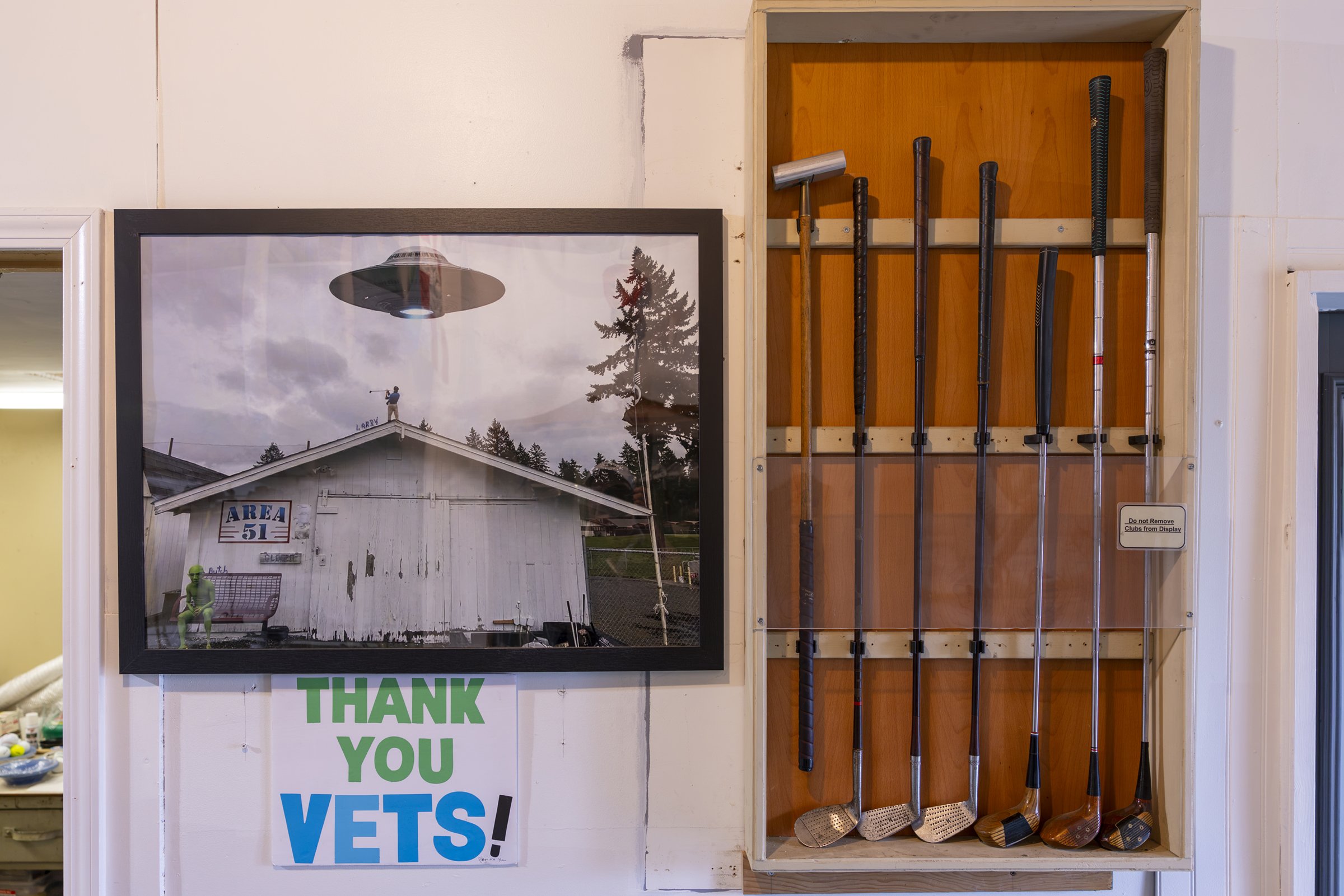 Framed UFO artwork, vintage golf clubs and a Thank You Vets sign on the Area 51 wall