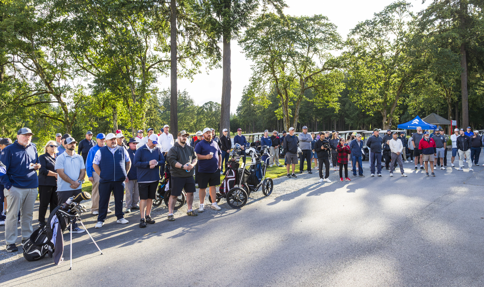 Golfers and guests gathered on the course under tall trees at an American Lake Veterans Golf Course event.