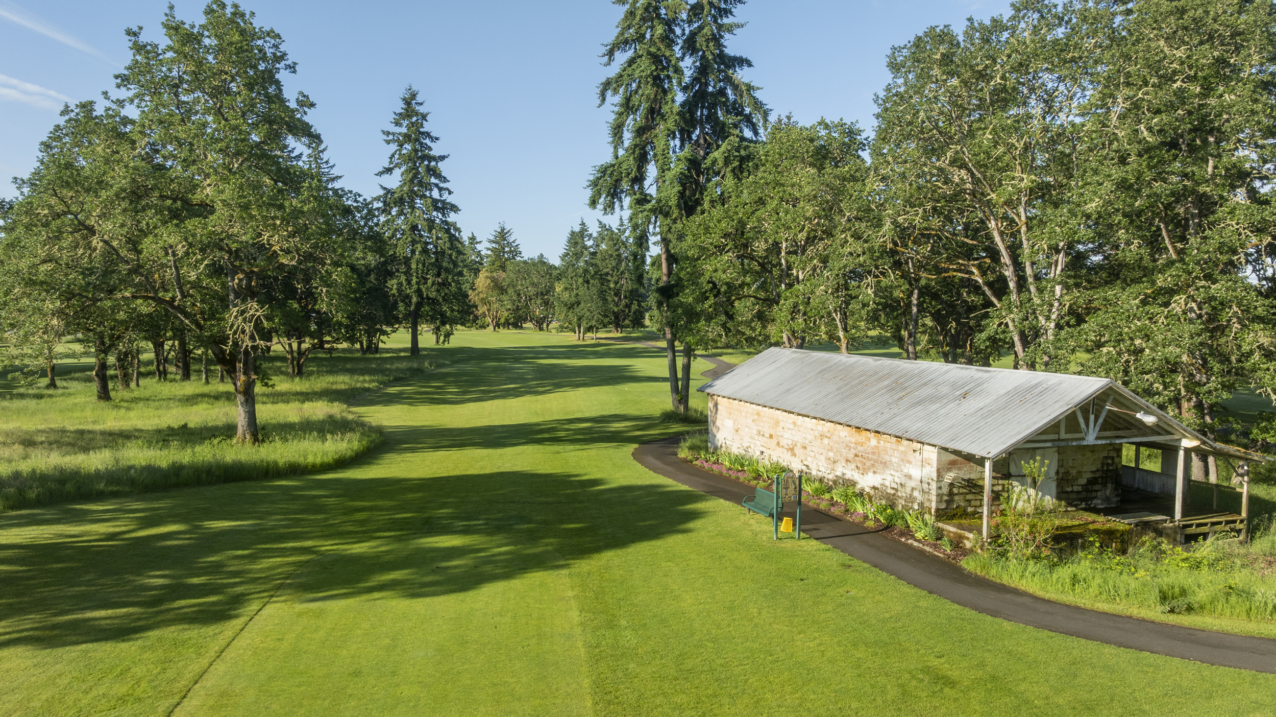 View from the Hole 18 tee at American Lake Veterans Golf Course, with a winding path and a stone building.