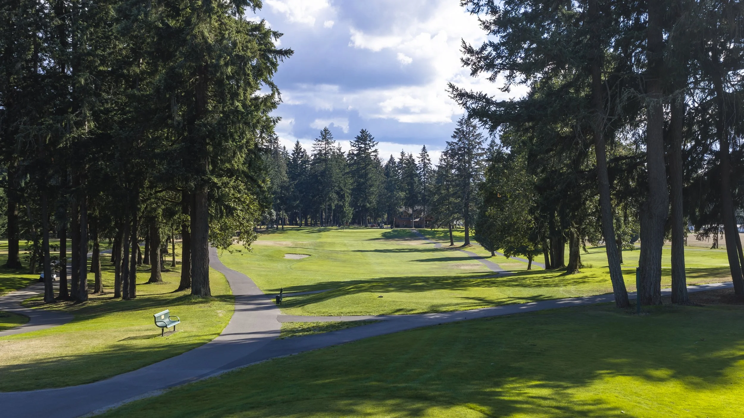 Hole 9 at American Lake Veterans Golf Course, framed by tall pines with a path and a bench.