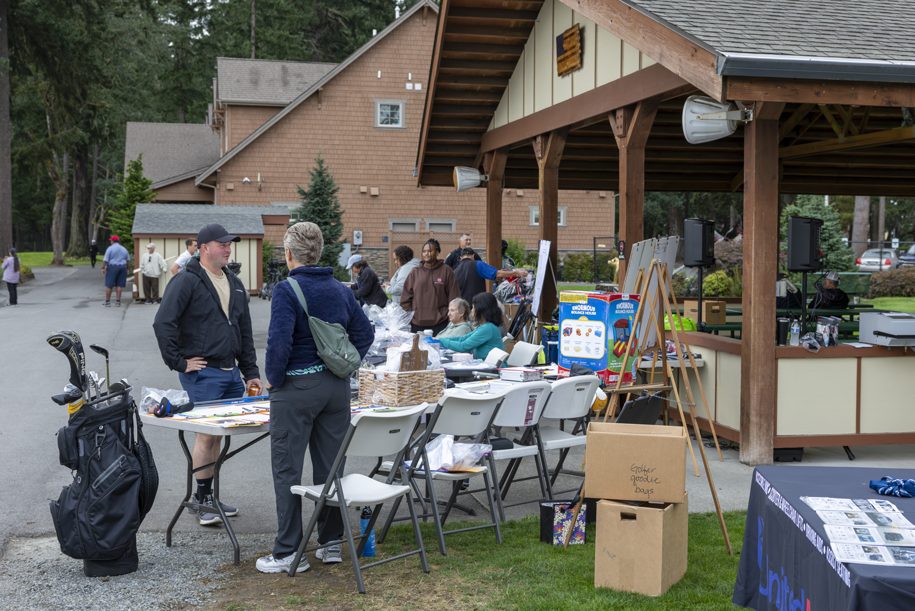 People browsing tables of golf clubs and other items outdoors at American Lake Veterans Golf Course.