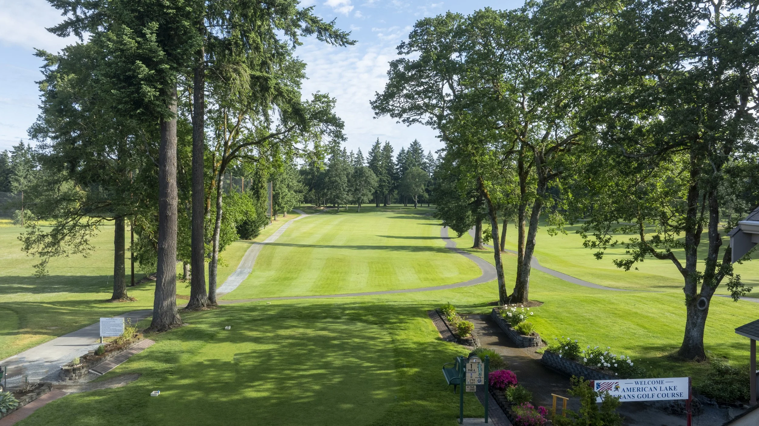 Hole 1 at American Lake Veterans Golf Course, a tree-lined fairway with a welcome sign.