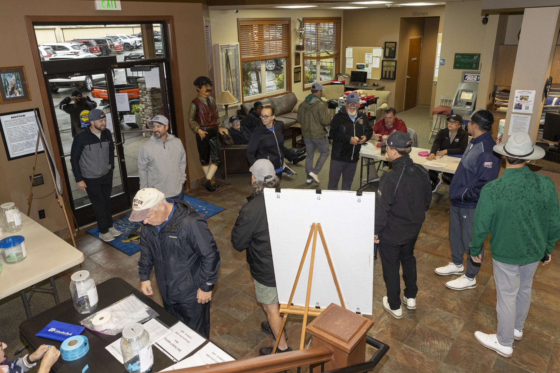 A group of people gathered indoors at American Lake Veterans Golf Course, some standing and some seated.