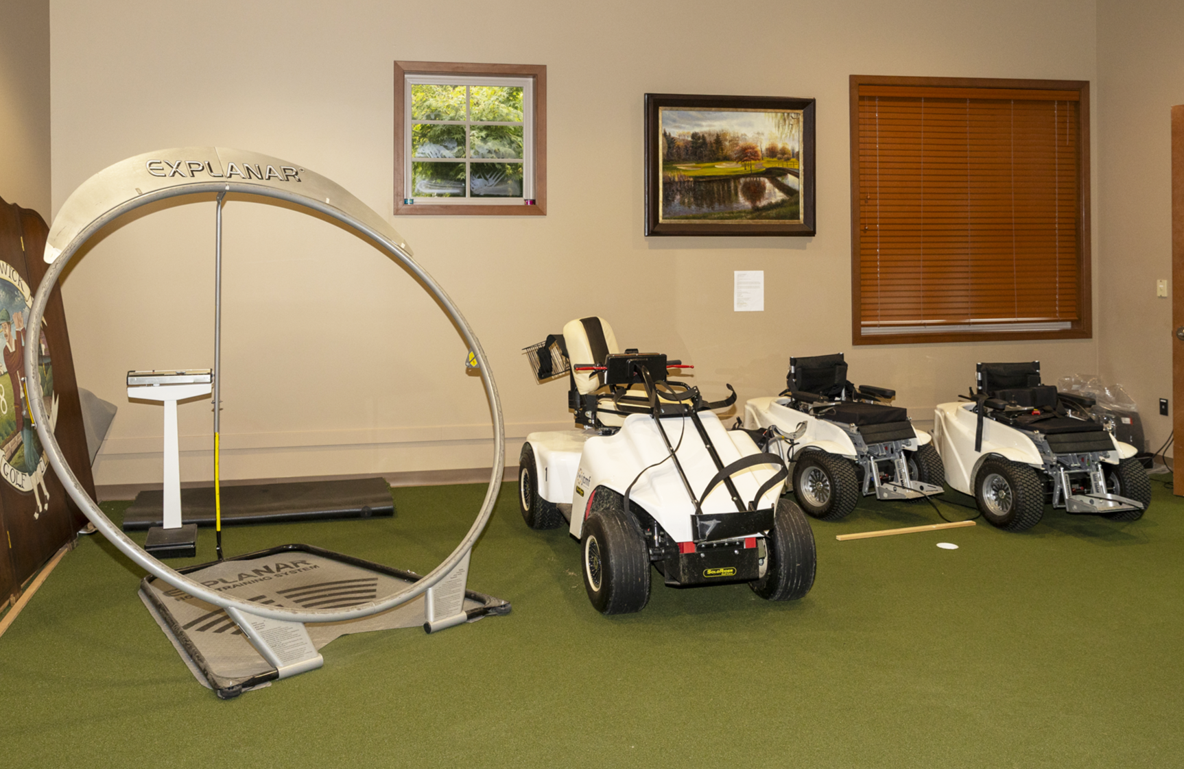 Indoor practice room with golf carts, a hitting station and a circular swing trainer.