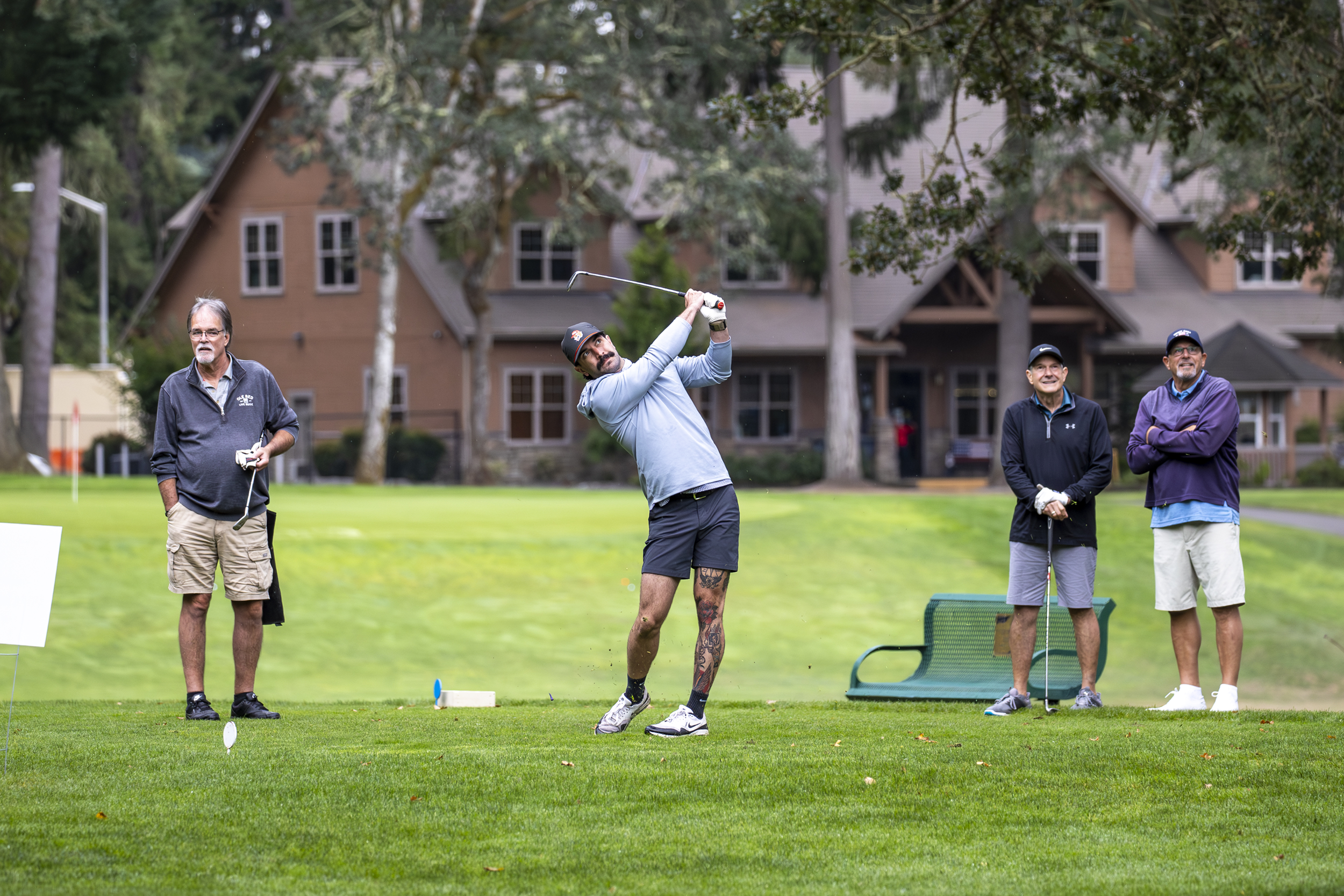 A golfer swings while three others watch on the course.
