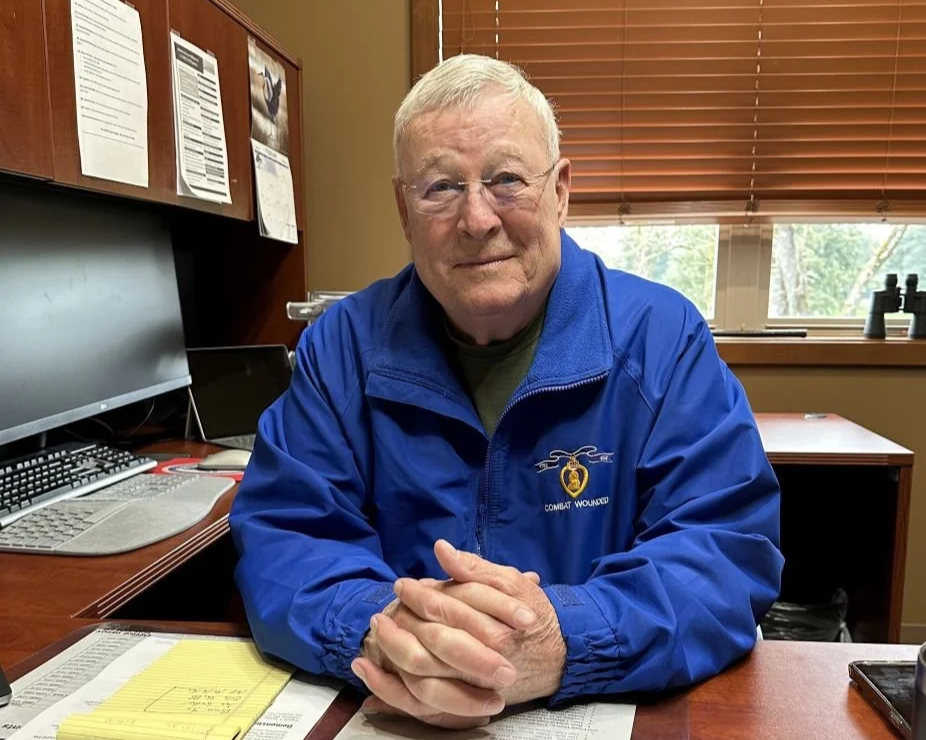Bruce McKenty seated at his desk in the American Lake Veterans Golf Course office, wearing a blue jacket.
