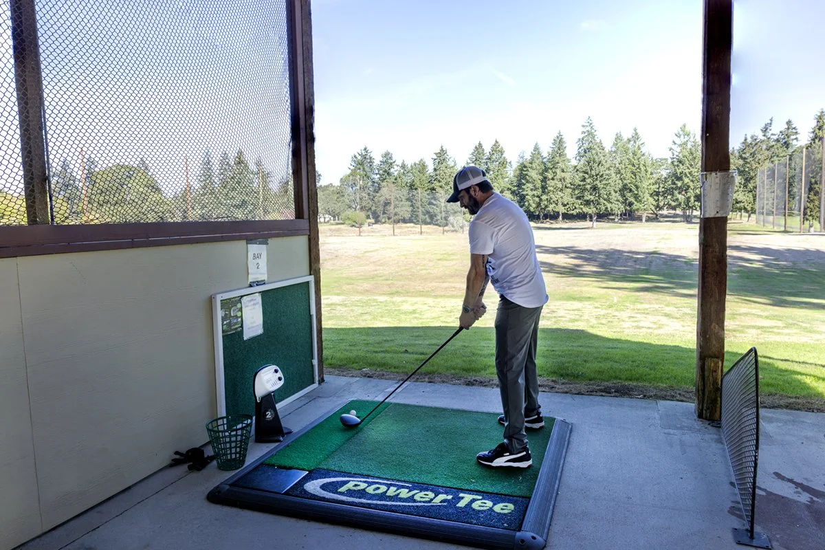 A golfer practices on a Power Tee mat at the American Lake driving range.