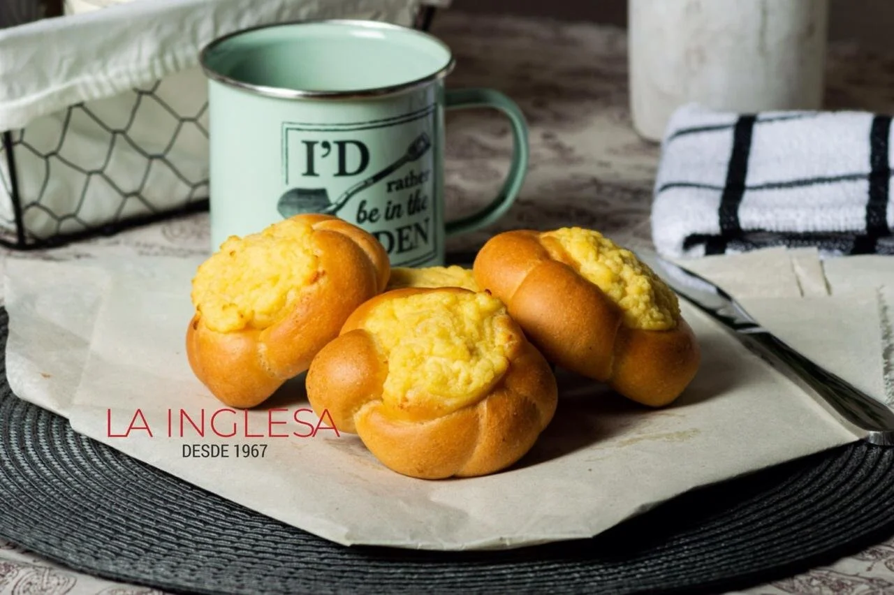 Cuatro panes aliñados tradicionales colombianos tipo Campesino en una bandeja con papel, acompañado de una taza de color verde con texto, un tenedor y una toalla de cocina de fondo.