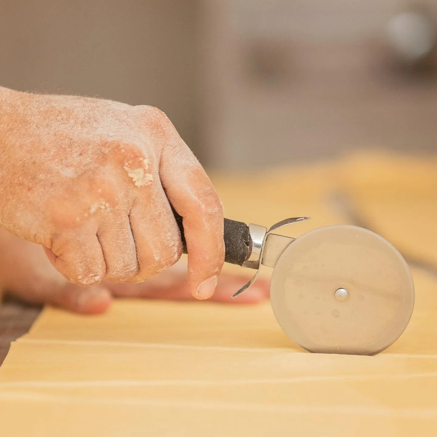 Mano sosteniendo un cortador de masa sobre una mesa de madera.