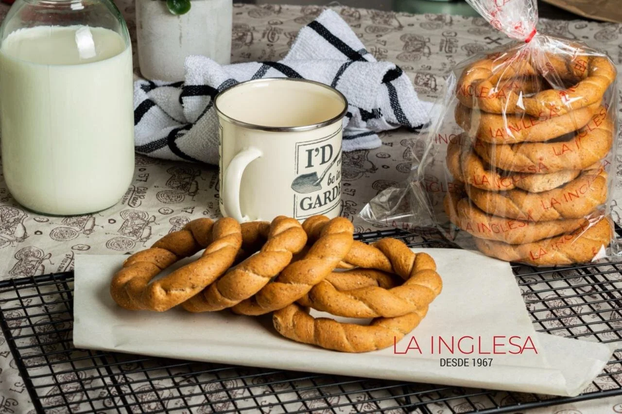 Tostadas en forma de trenza, una taza blanca con café, un frasco con leche, un paquete con más tostadas, una toalla y una rejilla para enfriar.