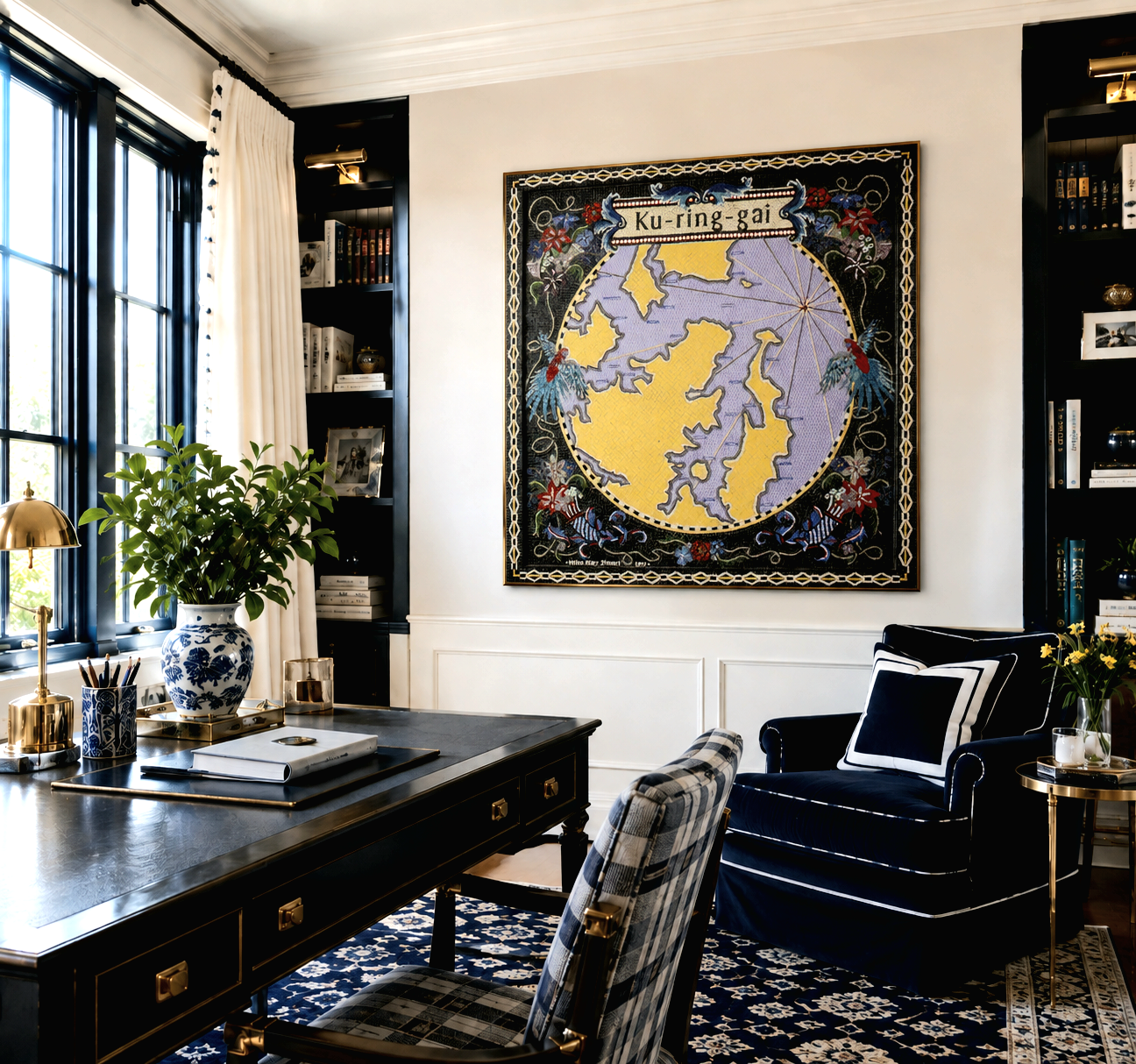 A home office with dark wood desk, plaid upholstered chair, black and white armchair, large framed map of the Arctic on the wall, bookshelf, window with white curtains, and decorative items including a large plant, lamp, and flowers.